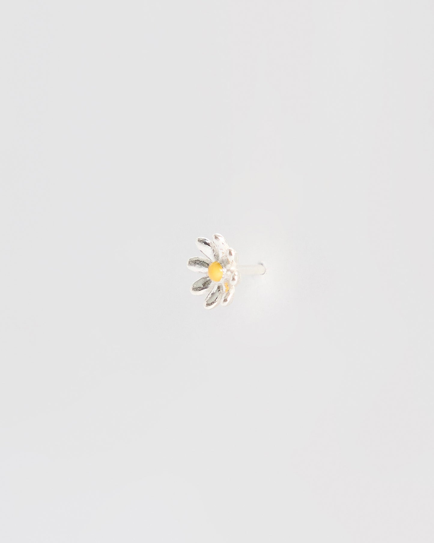 Side angle of a silver daisy stud earring showing the earring post and backing, with raised petal texture and a yellow enamel center.