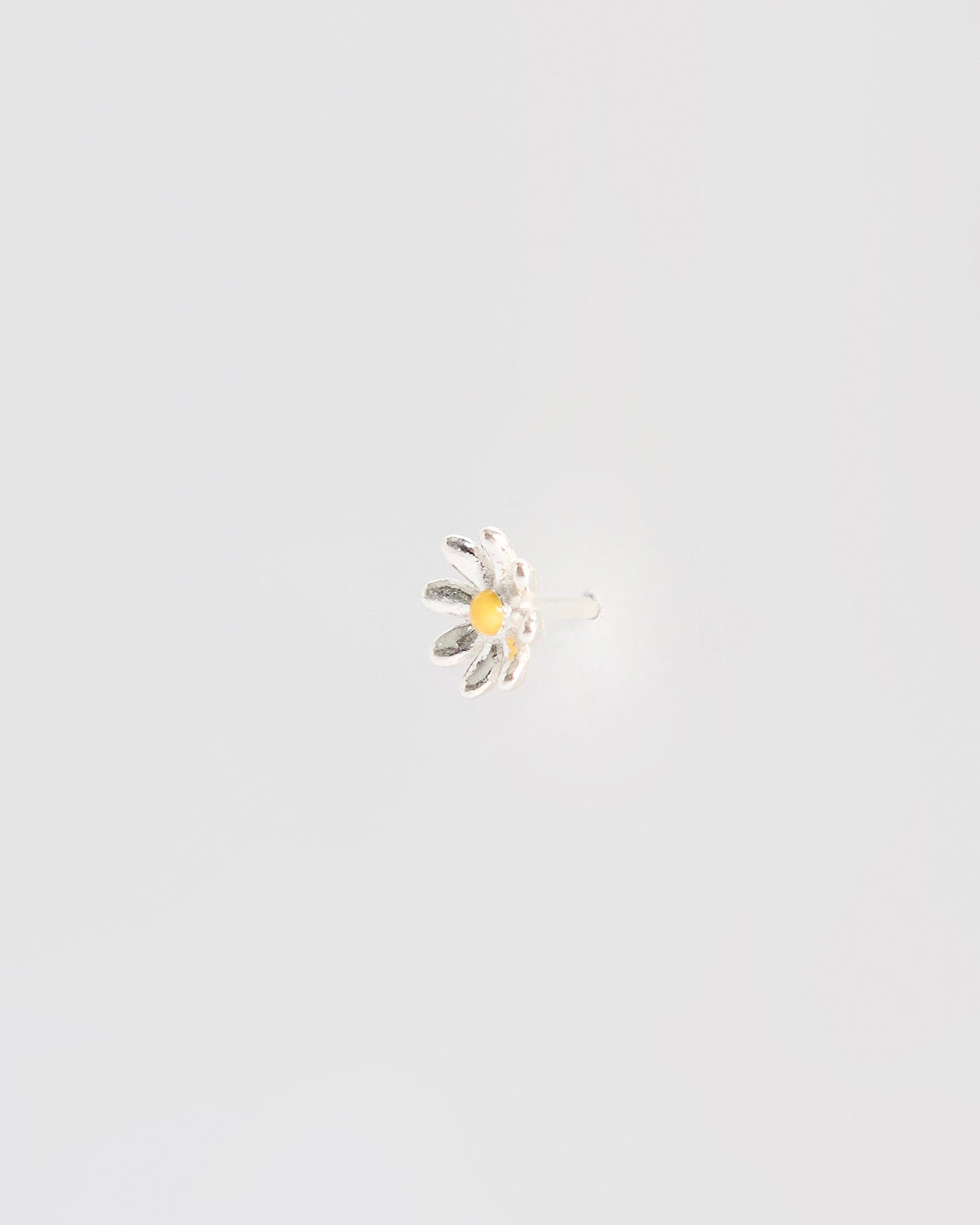 Side angle of a silver daisy stud earring showing the earring post and backing, with raised petal texture and a yellow enamel center.