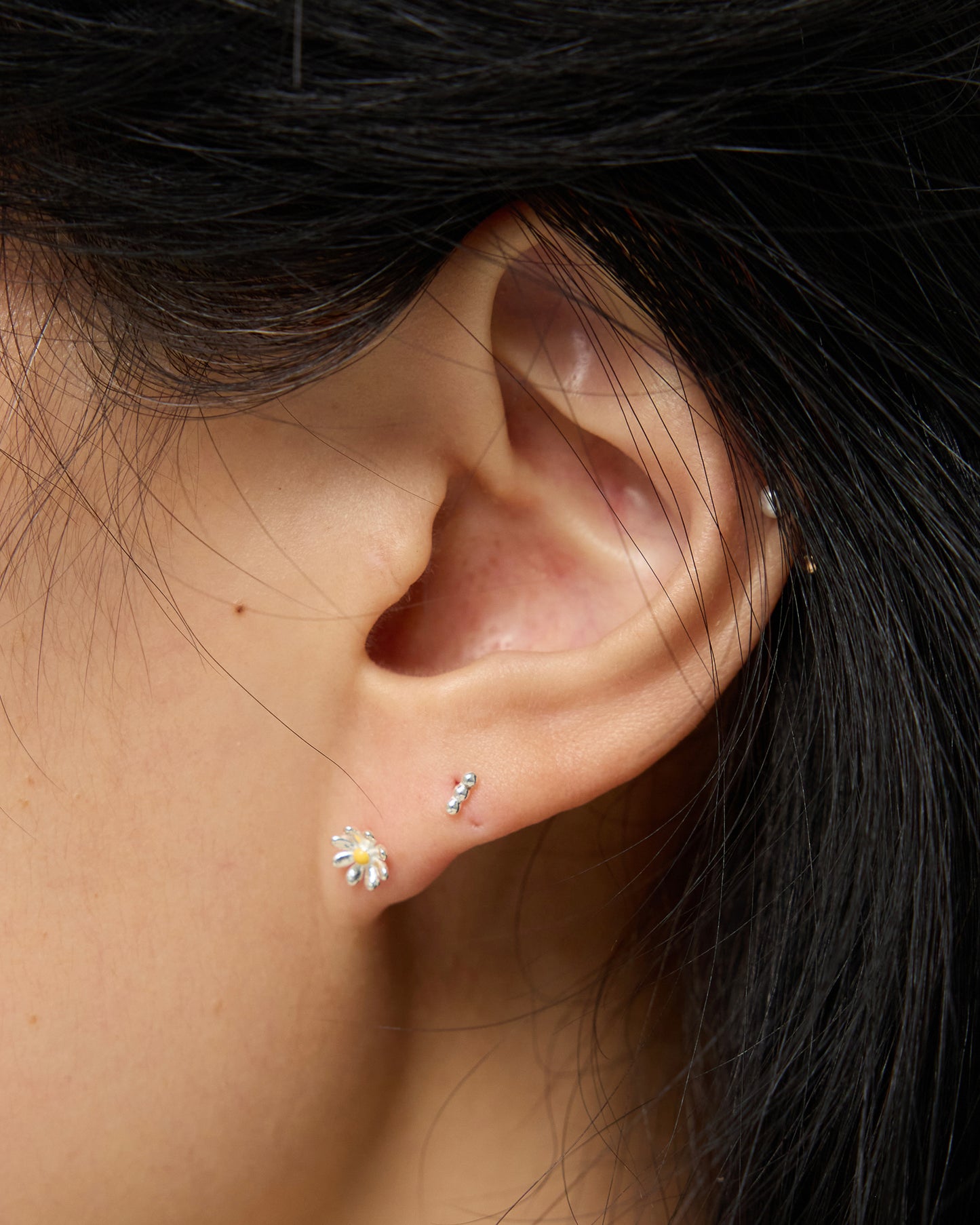Side profile of a model wearing a silver daisy stud earring with a yellow center, positioned neatly on the earlobe with a natural, casual hairstyle.