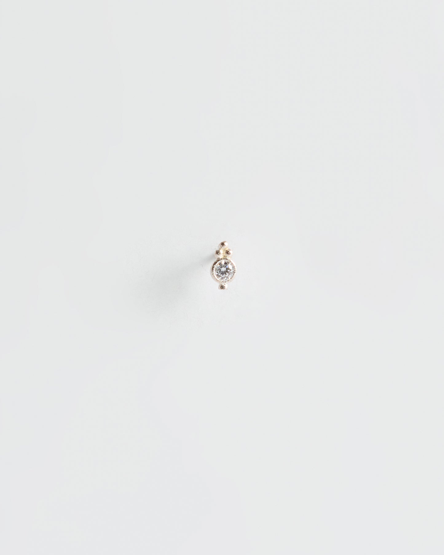 minimal silver stud earring resting in soft light, quiet and restrained composition