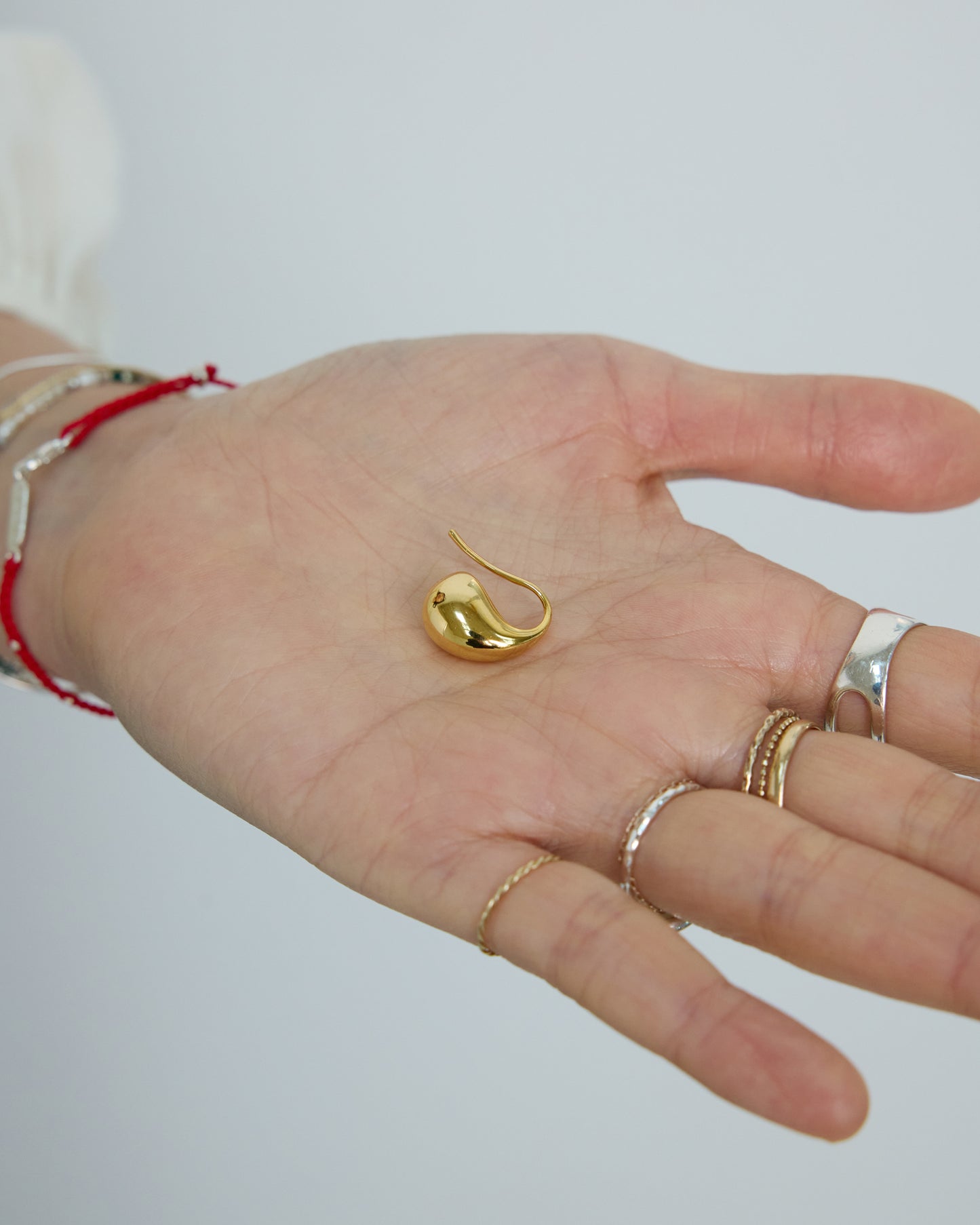 Gold fluid drop earring held in hand, showcasing polished finish and size