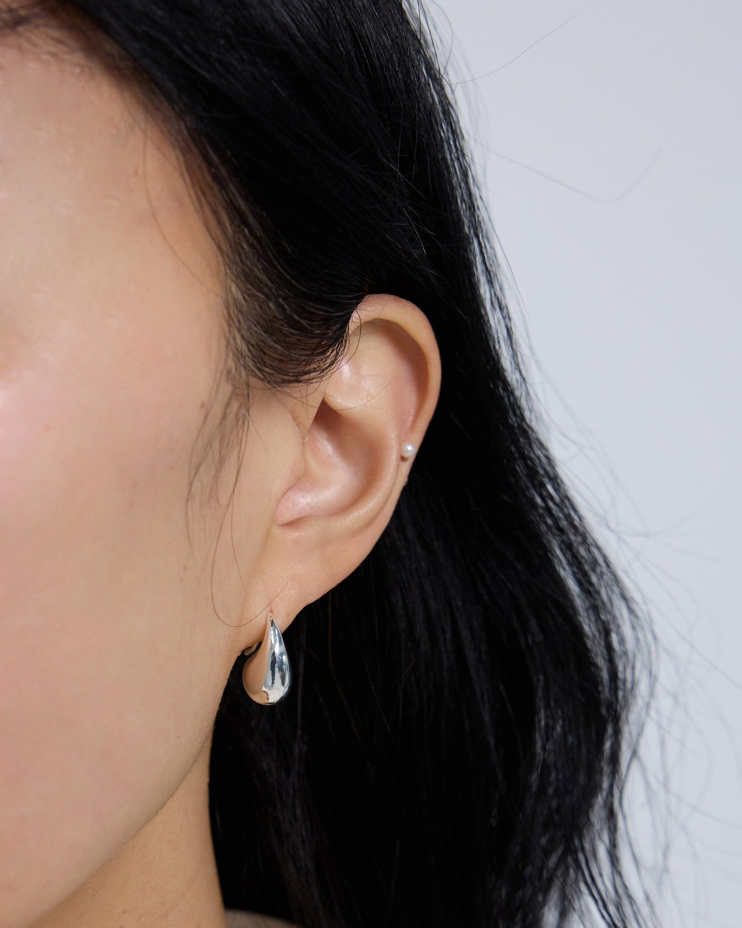 Silver fluid drop earrings worn on ear, minimalist curved statement earrings for everyday styling