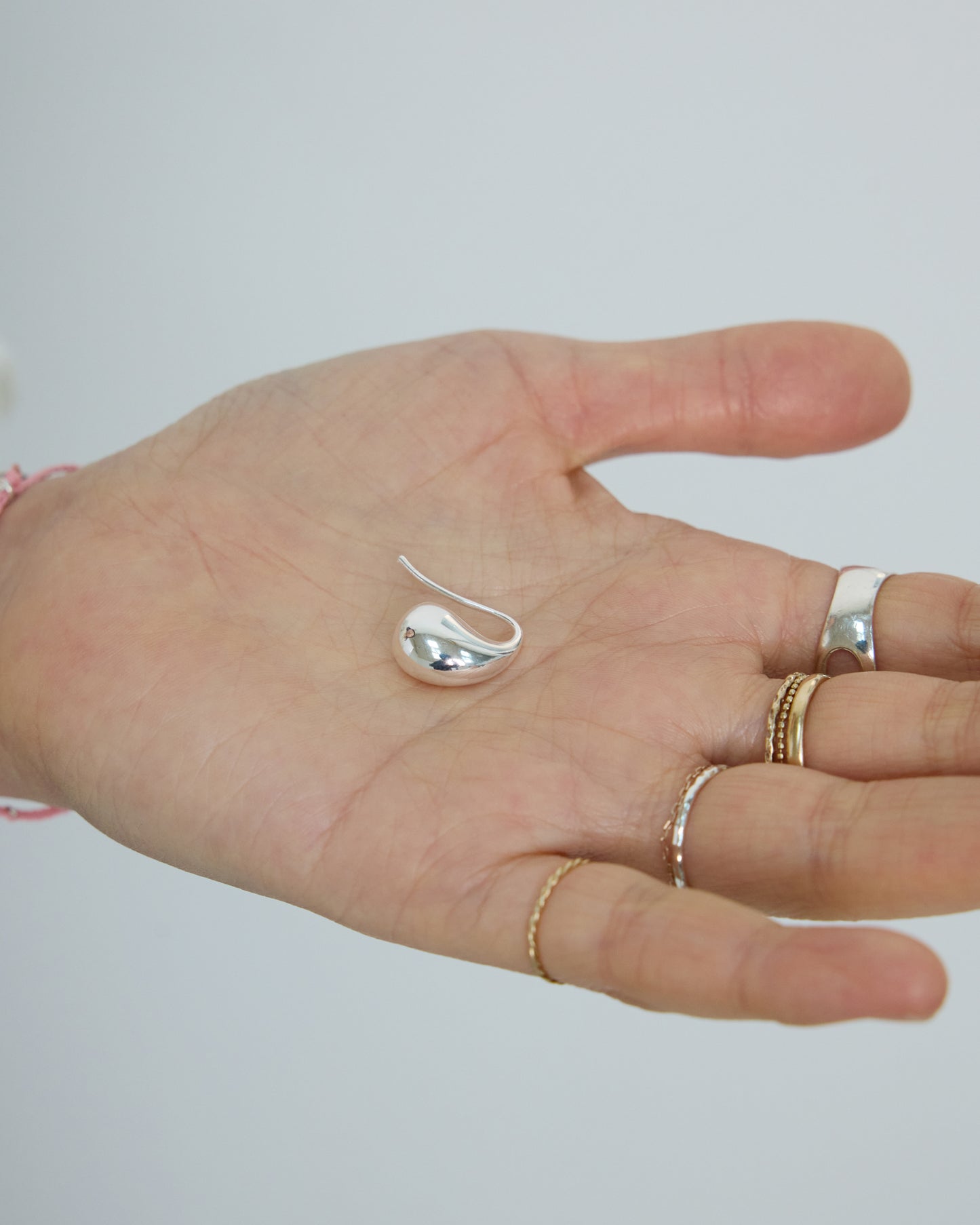 Hand holding a HANNA543 silver bold teardrop earring with layered silver and gold rings, demonstrating the K-style layering trend.