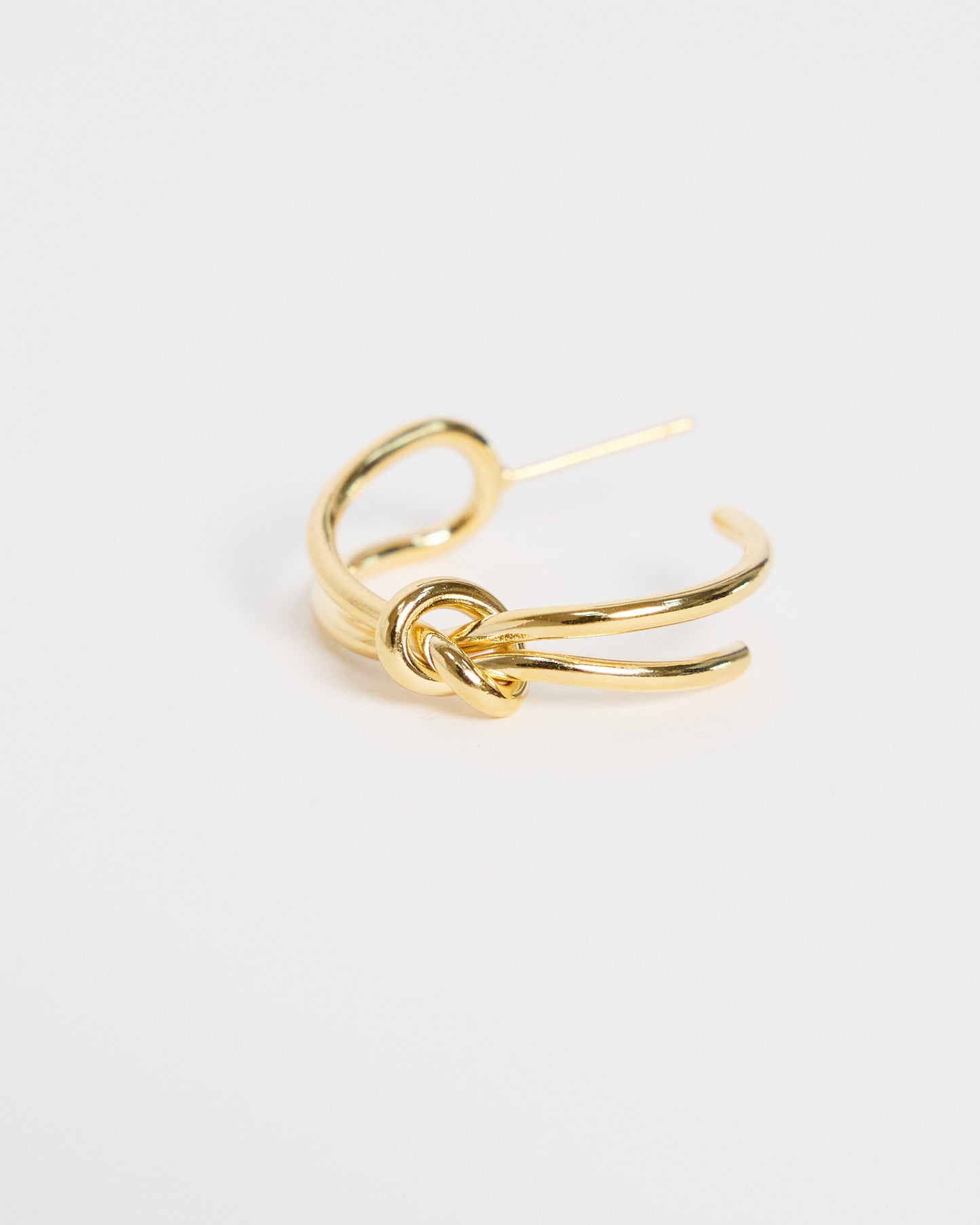 gold knot-shaped earring on a light gray background