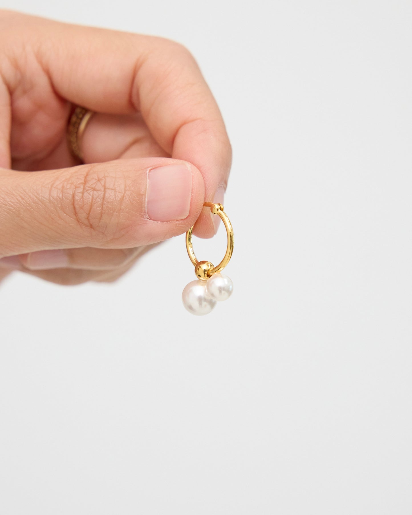 Close-up of fingers holding a gold-tone hoop earring with a rounded gold bead and two white pearls, highlighting the polished finish and delicate hanging detail.