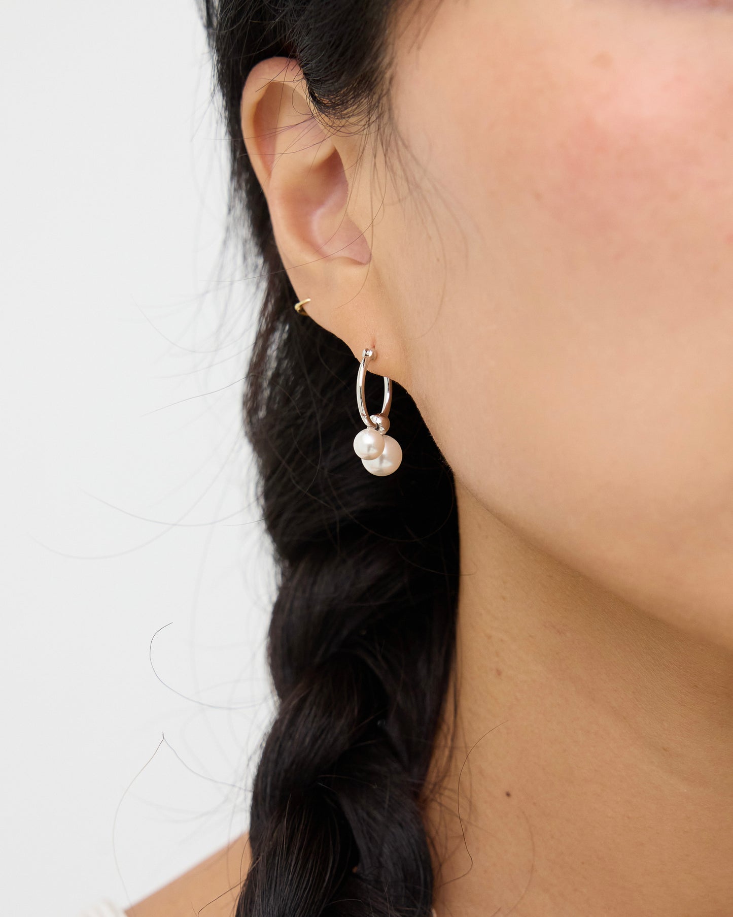 Model wearing silver-tone hoop earrings with two white pearl drops, shown from the side to highlight the size, shape, and movement of the pearls.