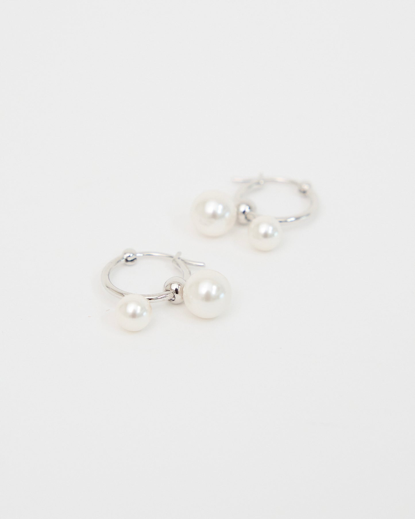 Front-facing product image of silver-tone hoop earrings with two white pearl drops, arranged neatly on a white background to show the full pair and balanced design.