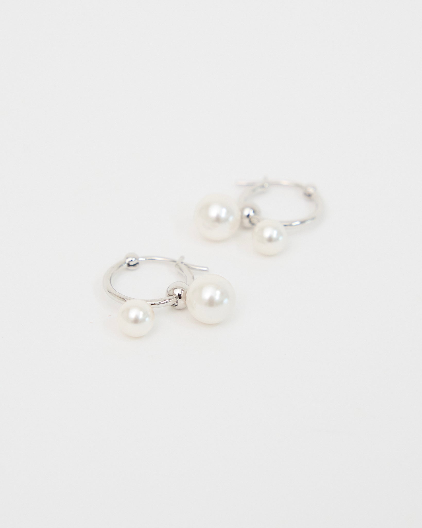 Front-facing product image of silver-tone hoop earrings with two white pearl drops, arranged neatly on a white background to show the full pair and balanced design.