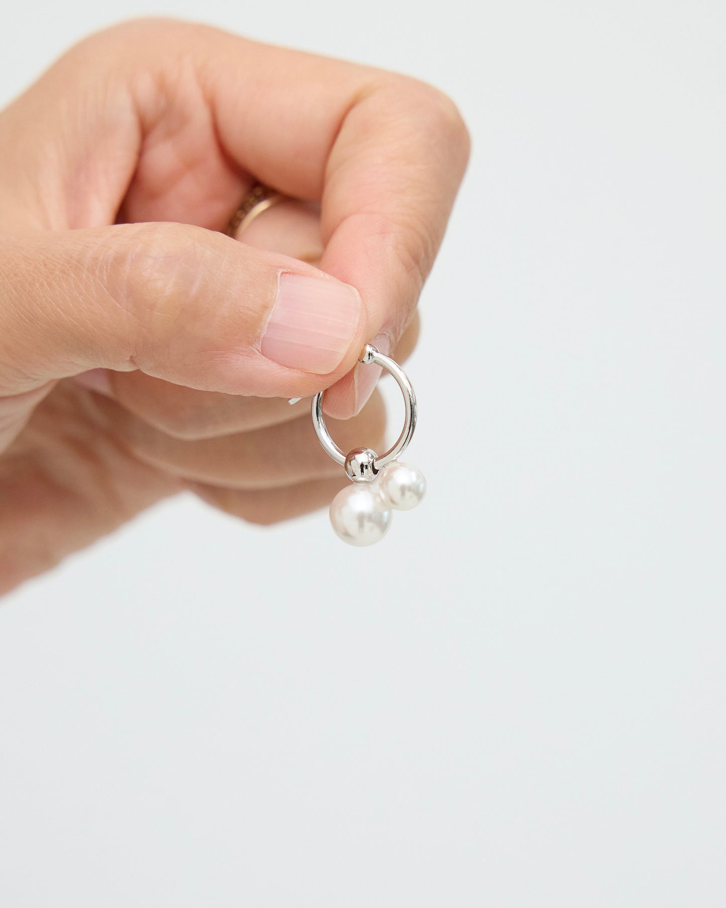 Close-up of fingers holding a silver-tone hoop earring with two white pearls, focusing on the curved hoop shape, polished metal surface, and pearl drop accents.