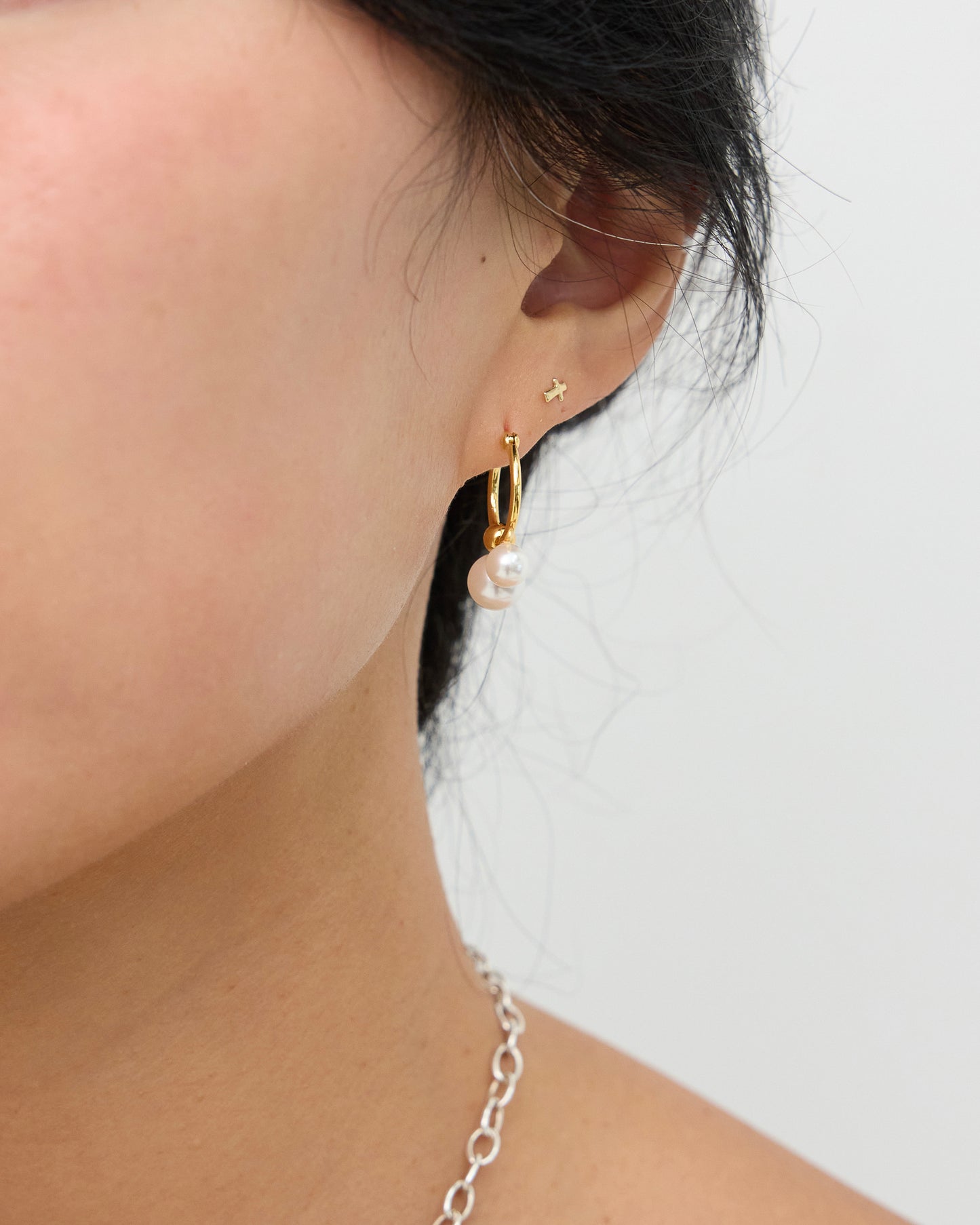 Side profile of a model wearing a gold-tone hoop earring with two white pearls hanging below the hoop, styled with additional small ear piercings.