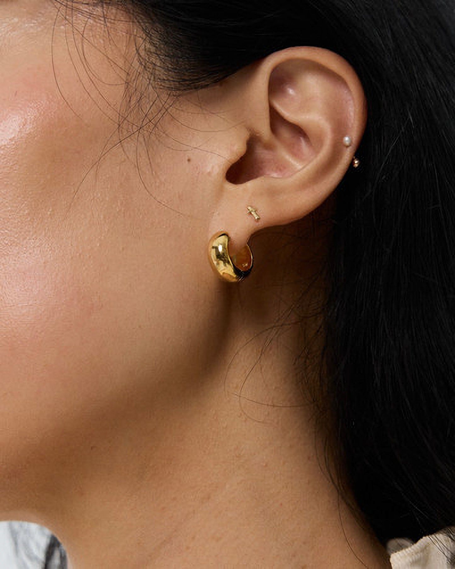 Close-up of an ear wearing gold hoop earrings with a blurred background