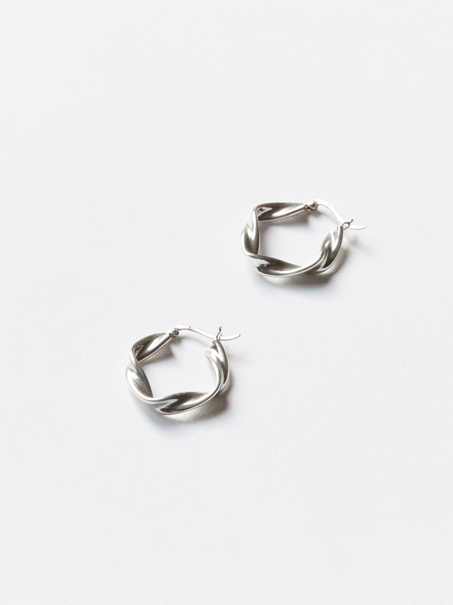 This image displays a pair of elegant silver earrings, known as the E510S. These earrings capture the graceful flow of nature with a design inspired by wind waves, embodying both softness and strength.