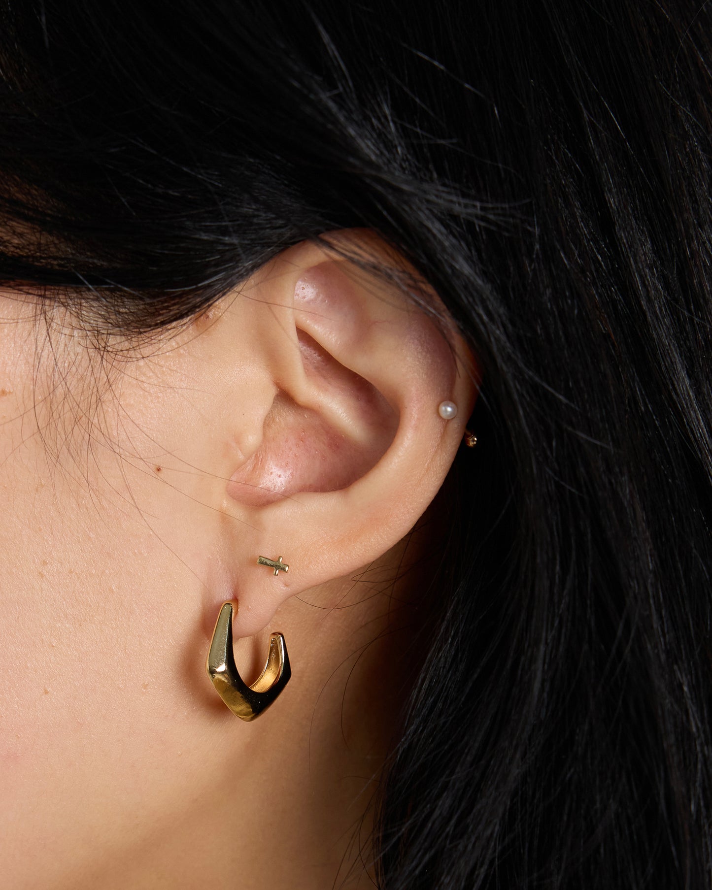 close up ear styling with gold chunky hoop and multiple piercings, modern layered earrings look