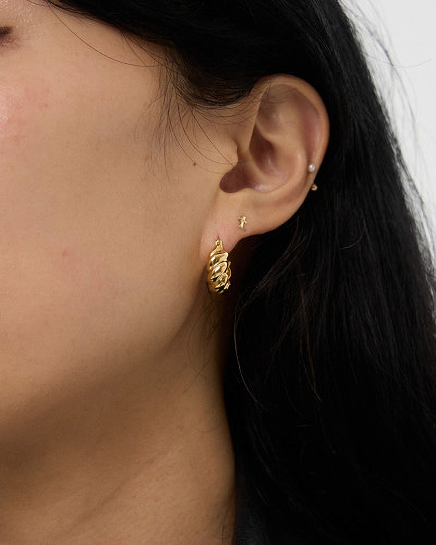 Close-up of an ear with gold hoop earrings and a small stud.