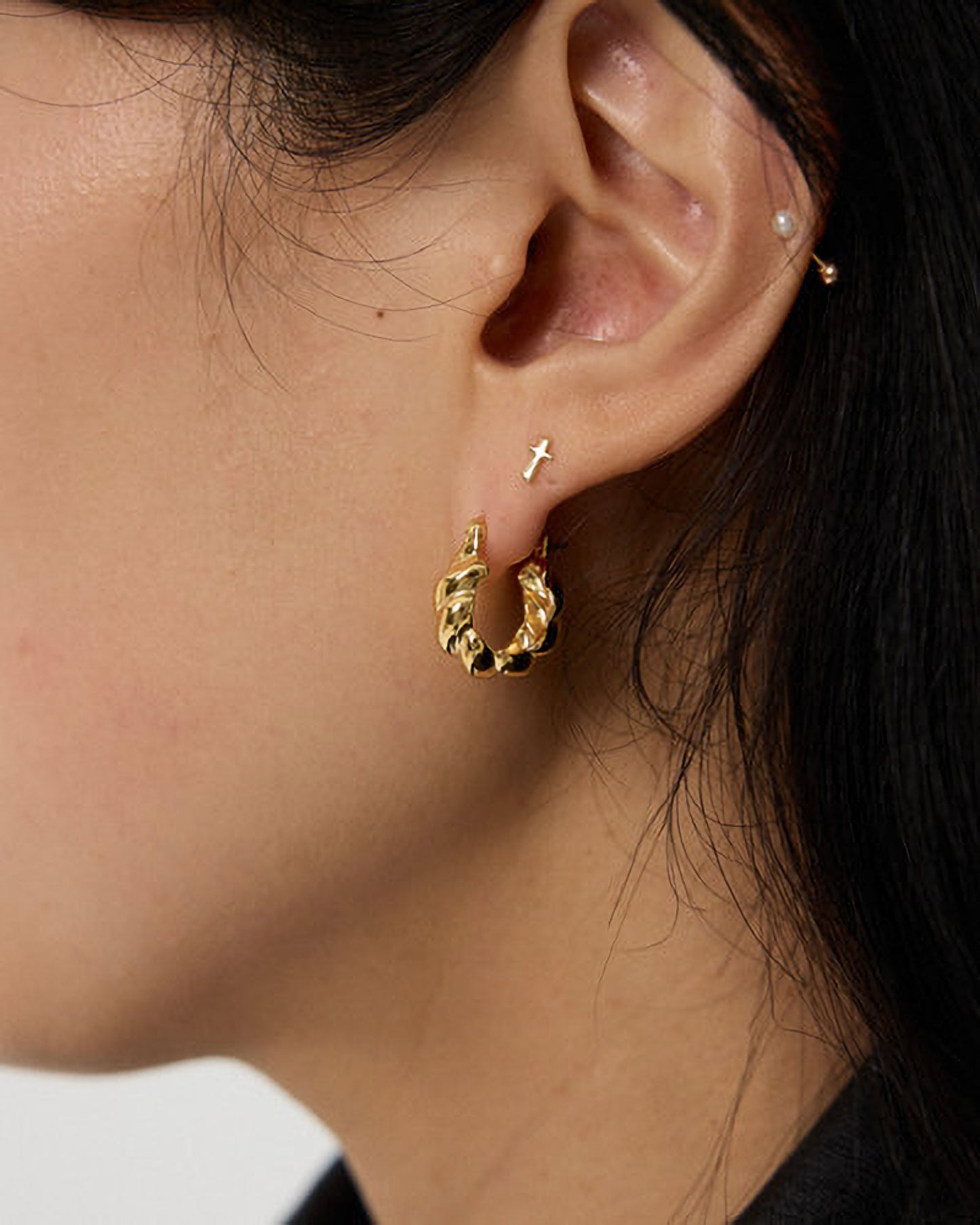 Close-up of a person wearing a gold hoop earring with a textured design.
