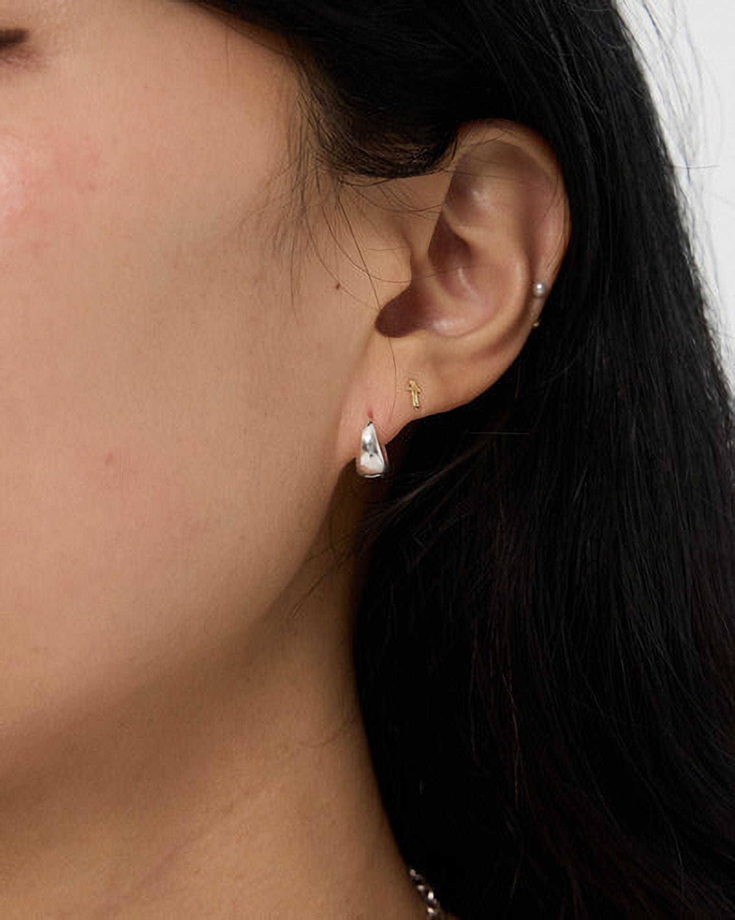 Close-up of an ear wearing a small earring with dark hair and skin background