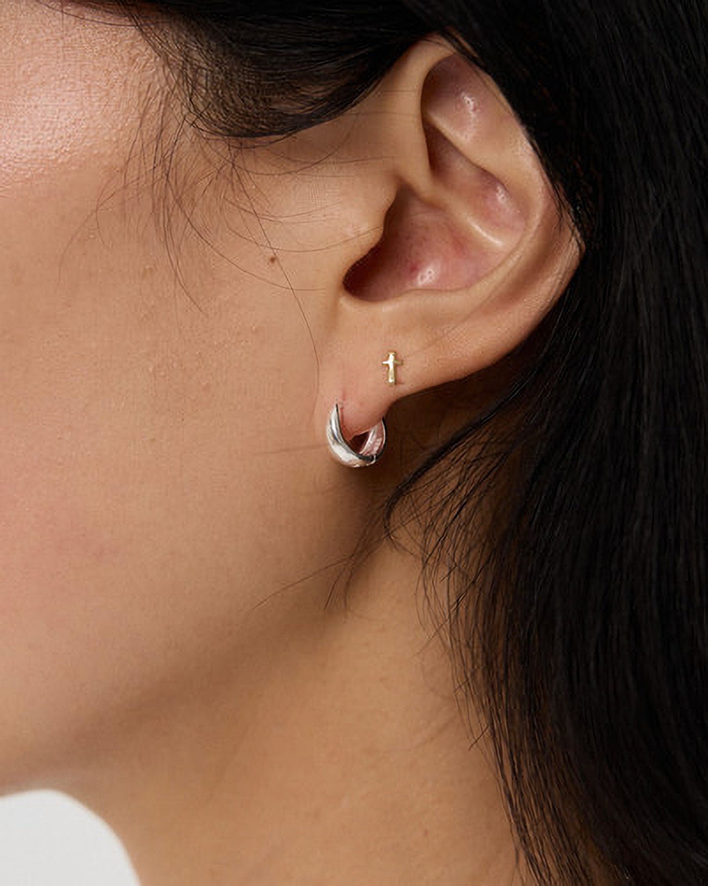 Close-up of an ear wearing a silver hoop earring with a cross charm.