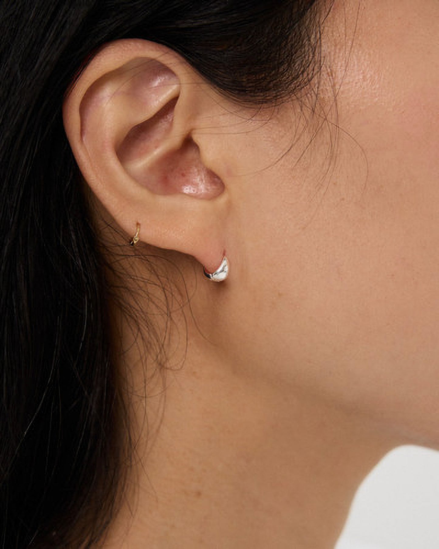 Close-up of an ear wearing a silver hoop earring with a blurred background