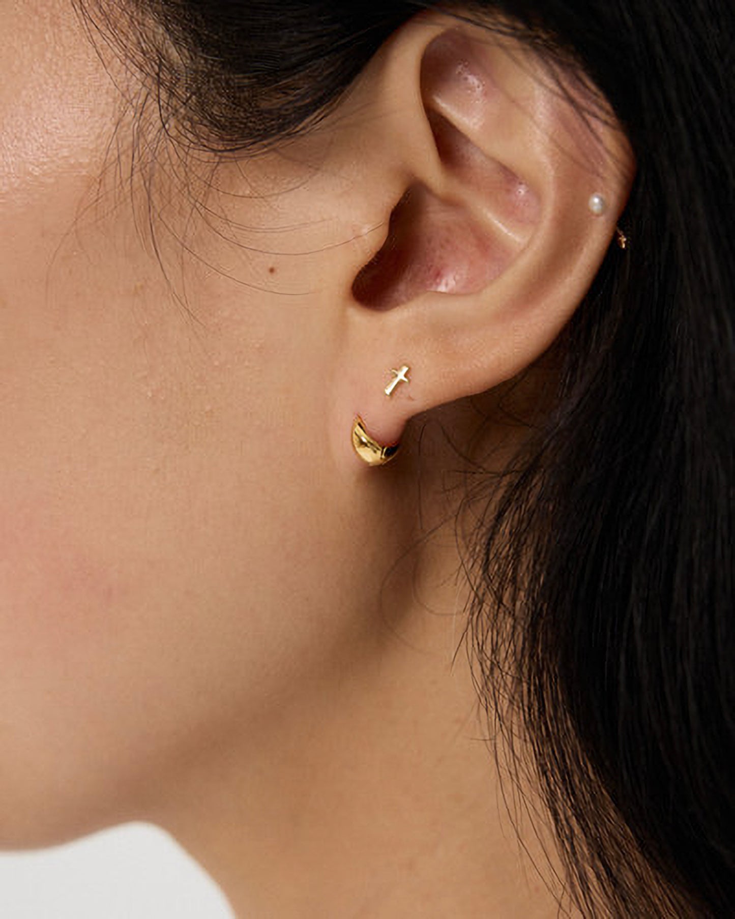 Close-up of an ear wearing gold hoop earrings with a minimal background