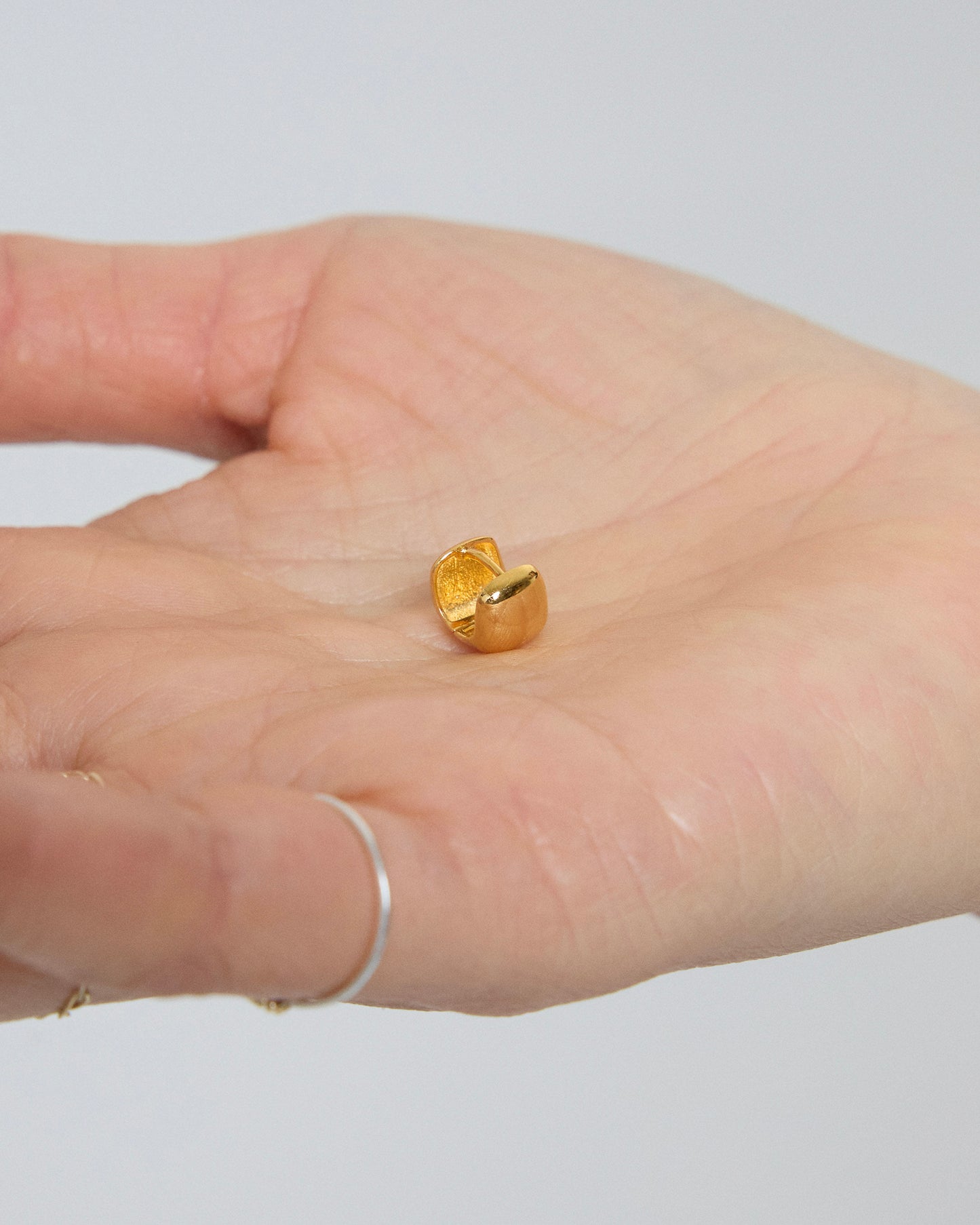 Gold earring on a person's hand with a plain background