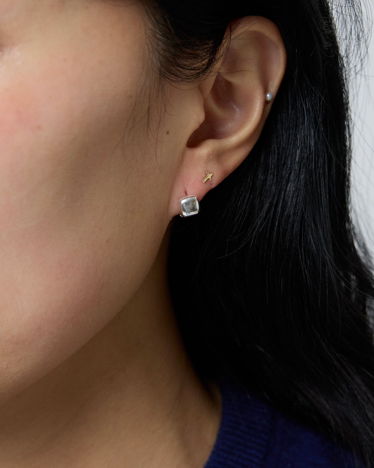 minimal silver square stud earrings worn on ear, polished rounded cube shape, modern everyday jewelry styling, sterling silver minimalist earring