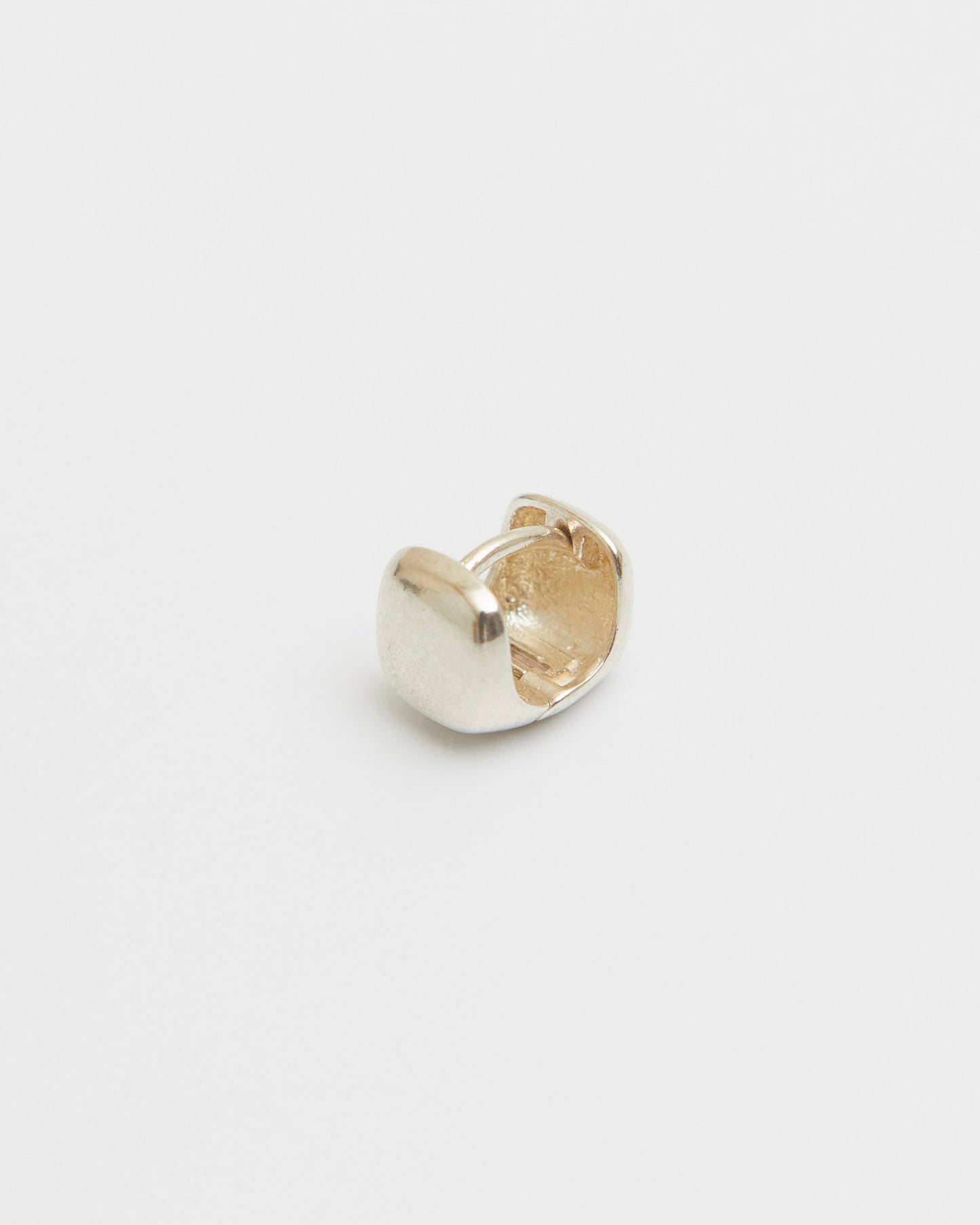 close-up of silver square stud earring in hand, rounded cube shape, polished surface, minimal jewelry detail
