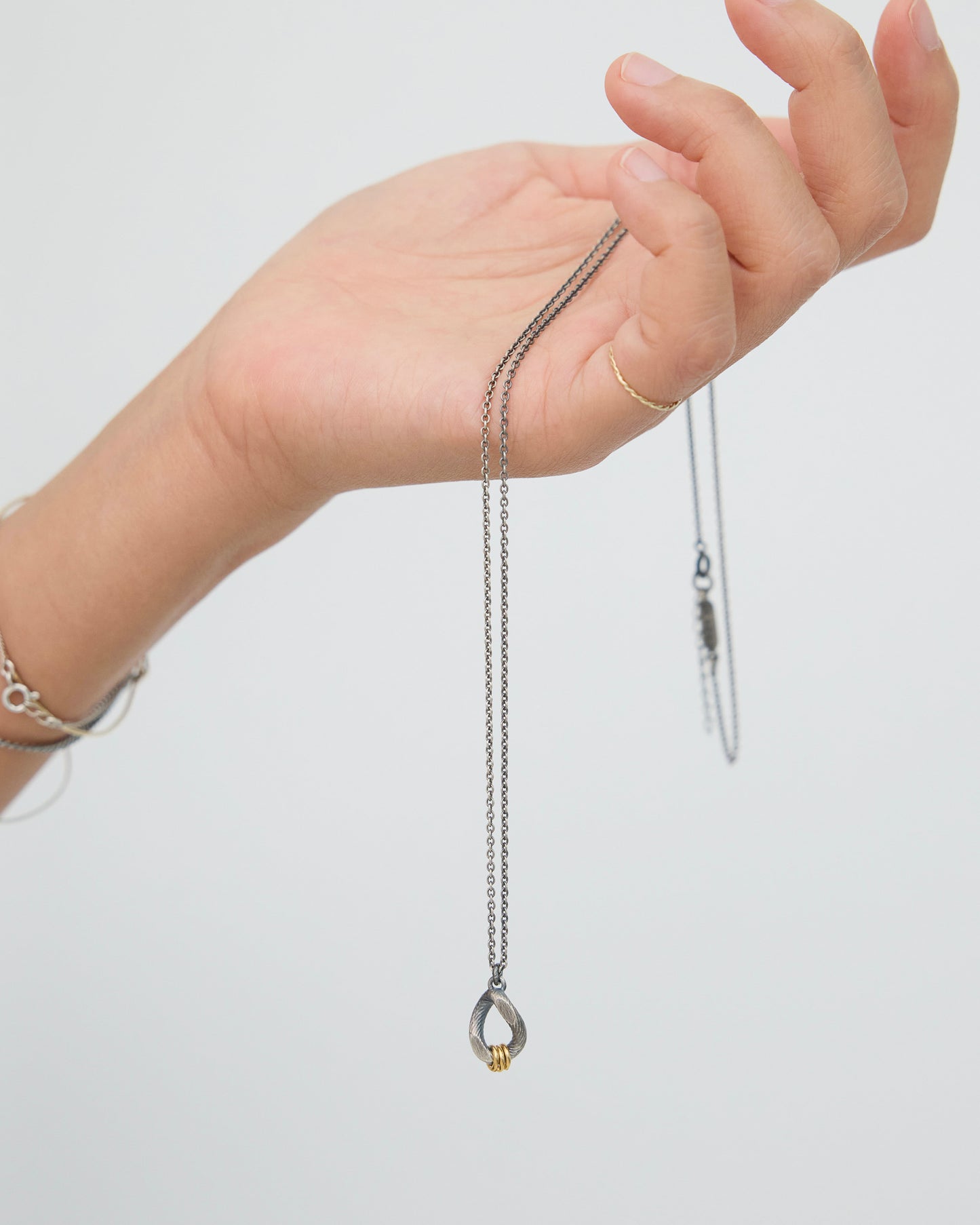 Hand holding a delicate antique silver necklace with a small gold pendant on a plain background