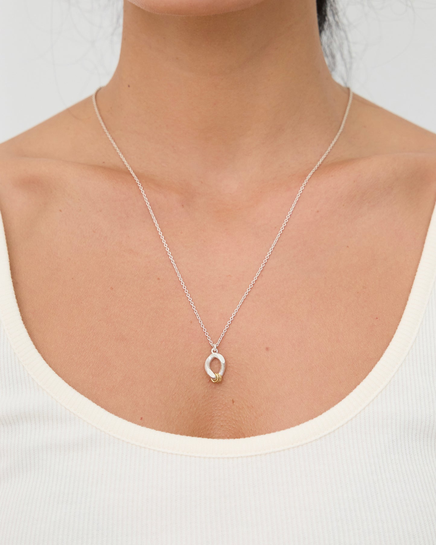 Woman wearing a sterling silver and gold mixed metal pendant necklace with white tank top