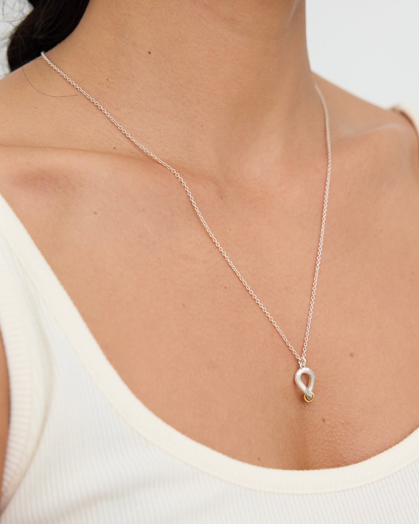 Close-up angled view of an organic silver pendant necklace with gold ring accents