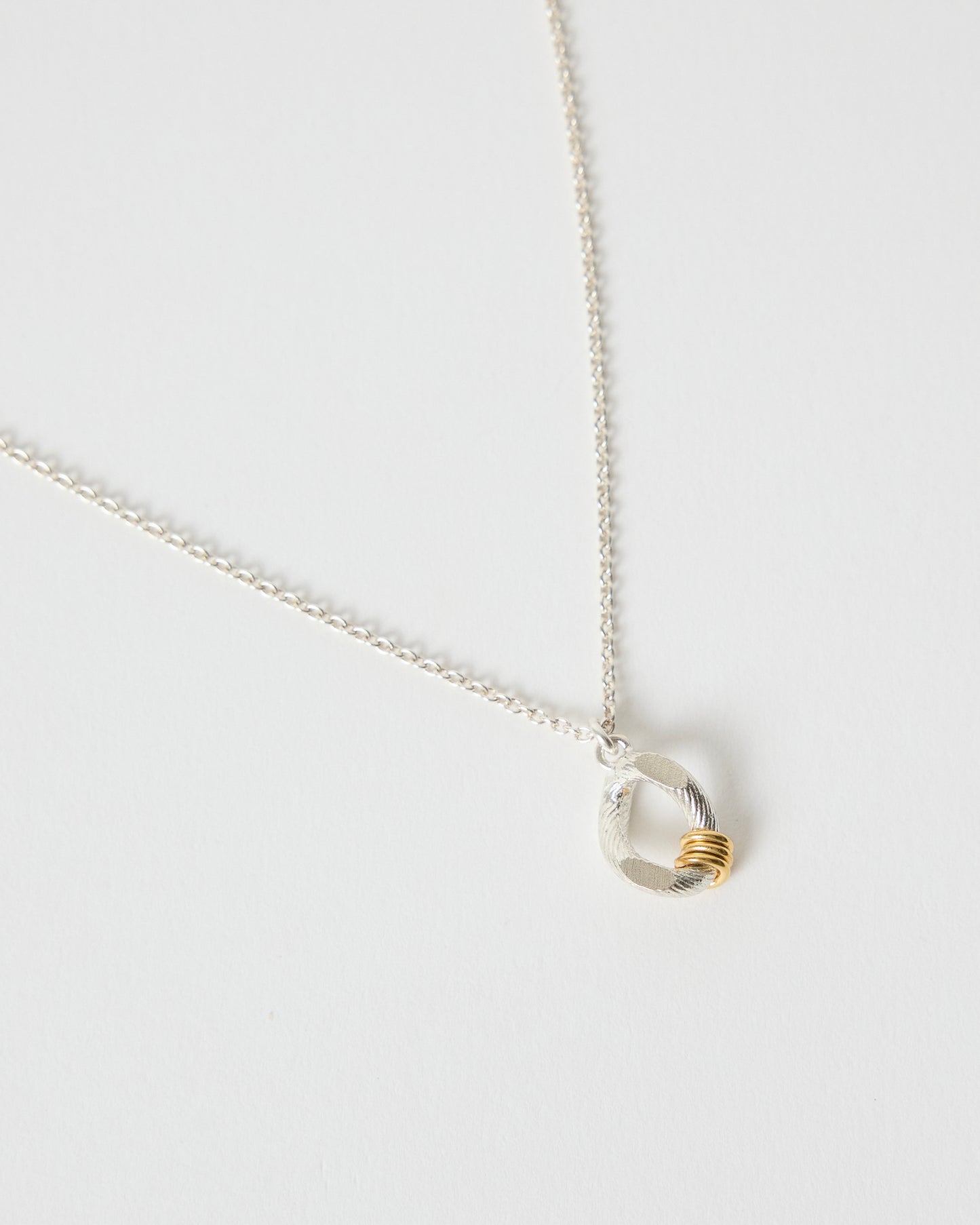 Close-up detail of textured sterling silver pendant with gold accent rings
