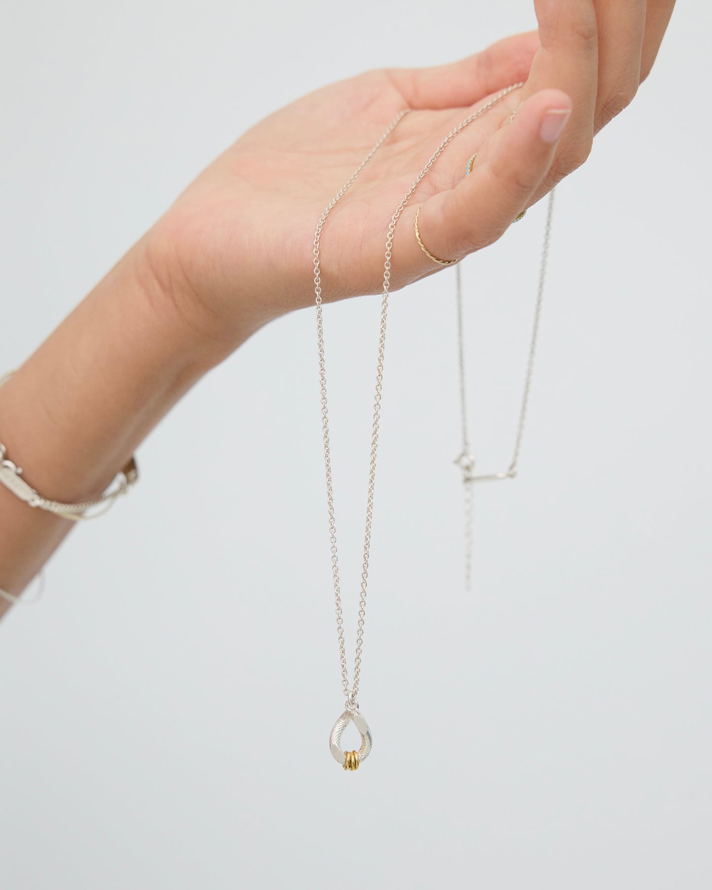 Hand holding sculptural mixed metal necklace showing pendant size and chain length