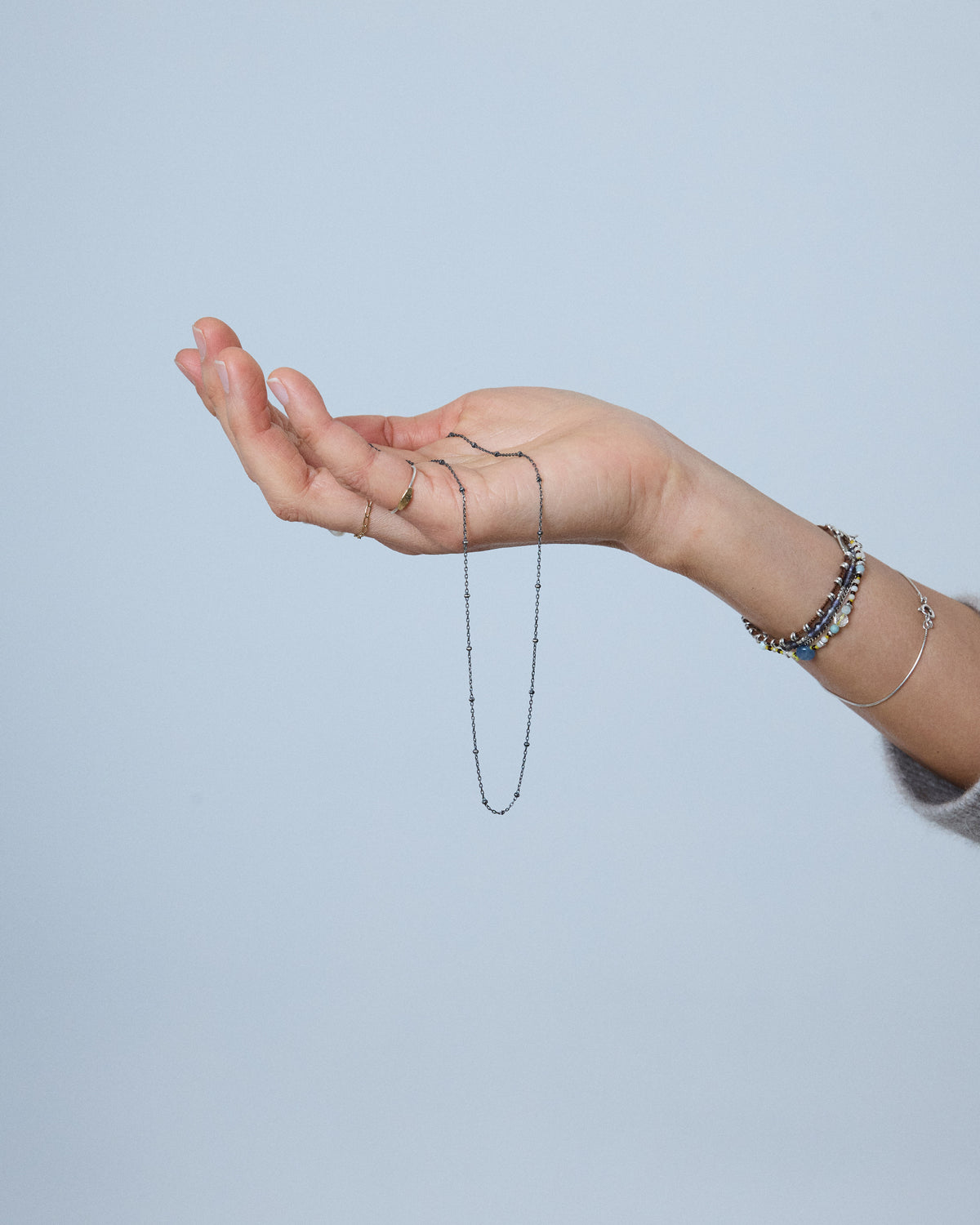 Hand holding an antique silver dot chain necklace against a soft blue background – HANNA543 N1057 starlit dot chain