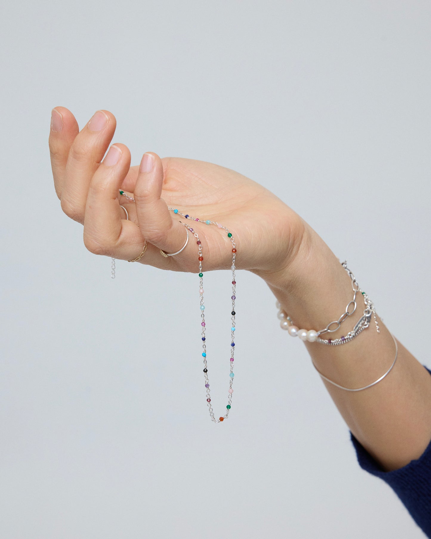 Hand holding sterling silver necklace with multicolored gemstone accents