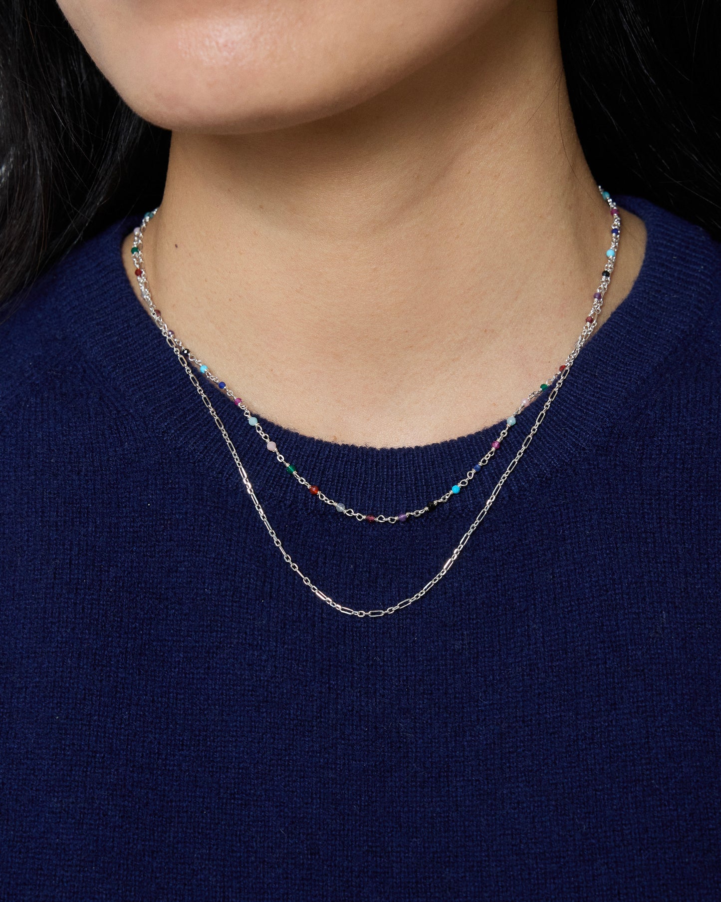 Woman wearing layered gemstone necklace with silver paperclip chain