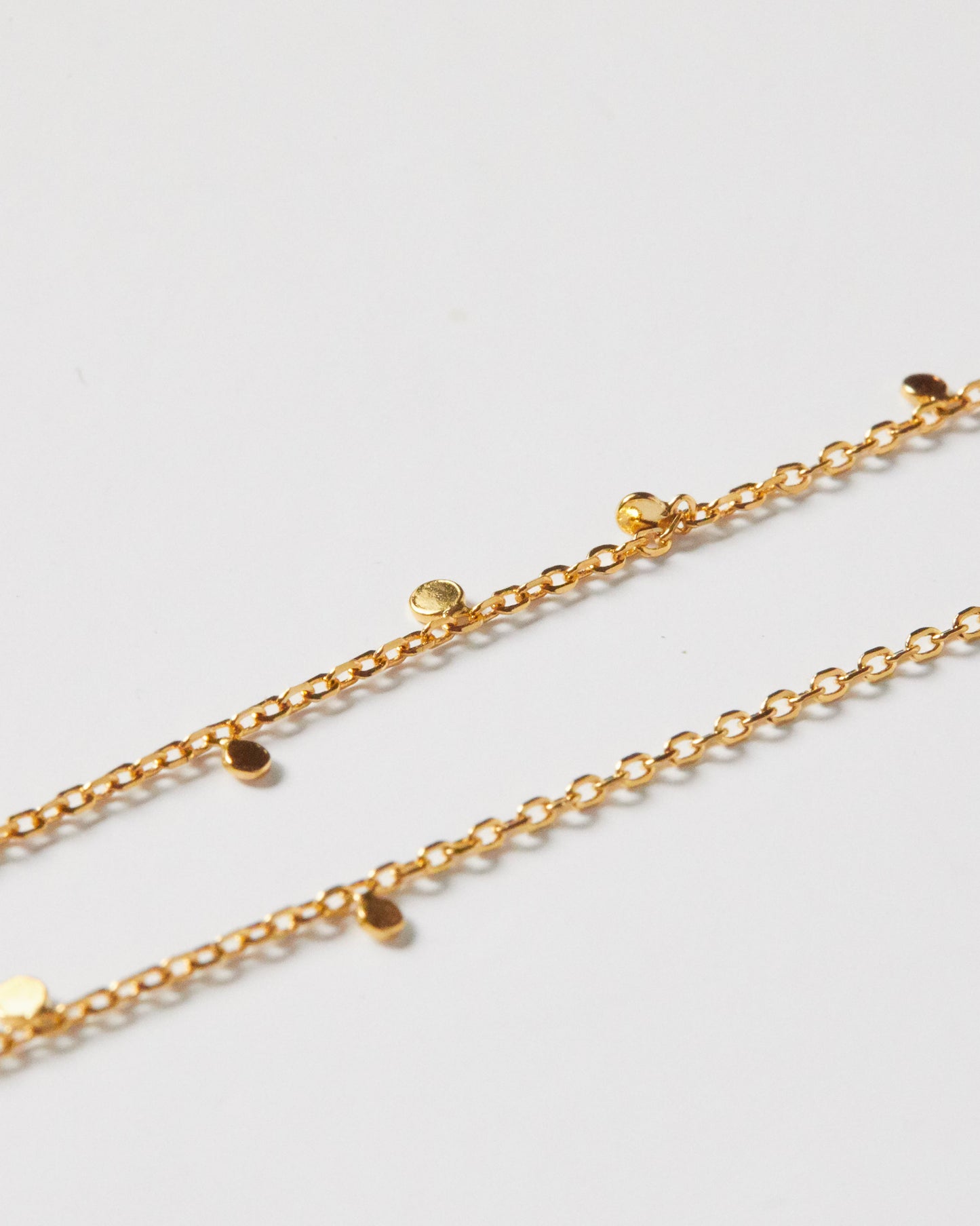Close-up detail of gold necklace with small disc charms on chain