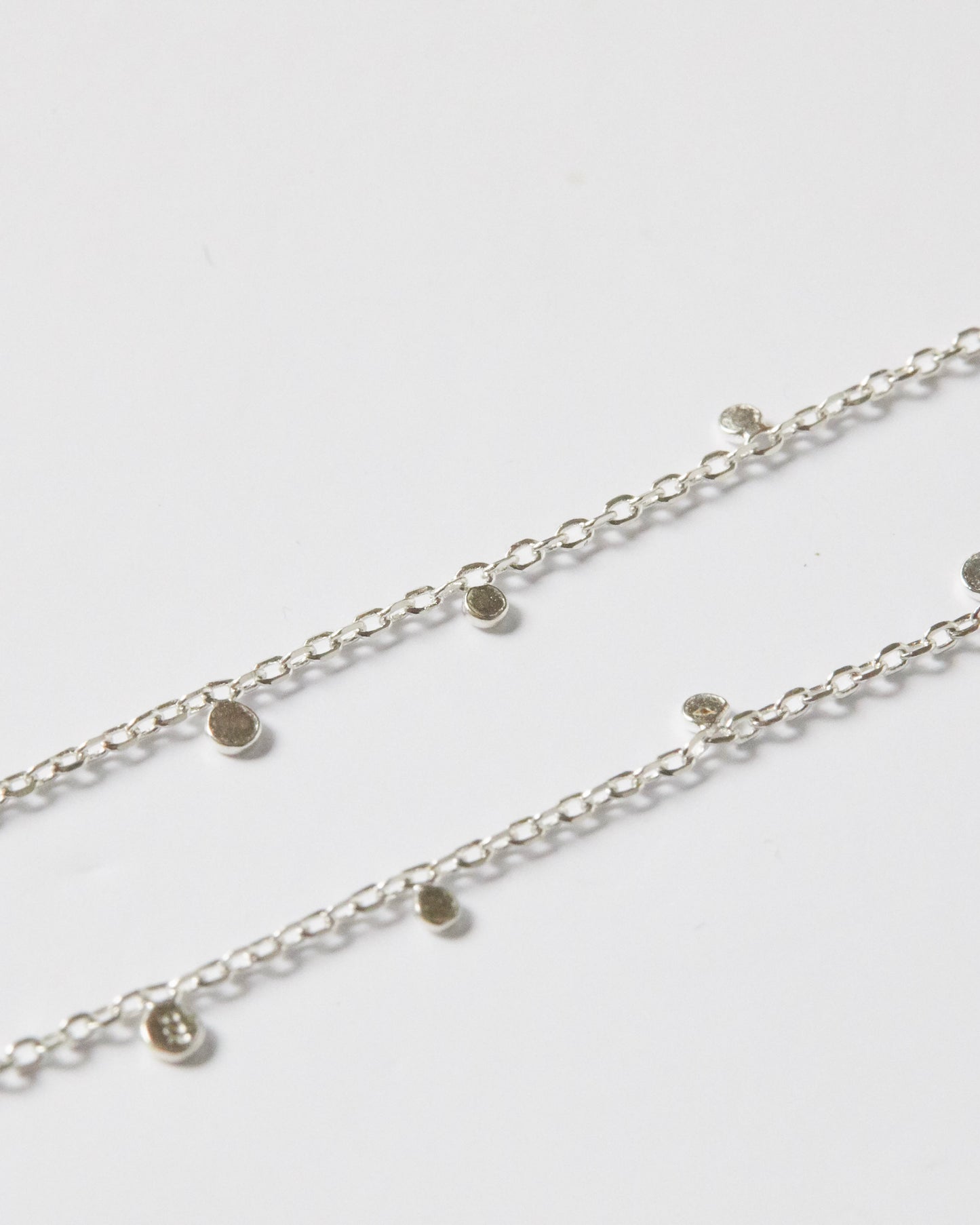 Close-up detail of silver necklace with small disc charms on chain