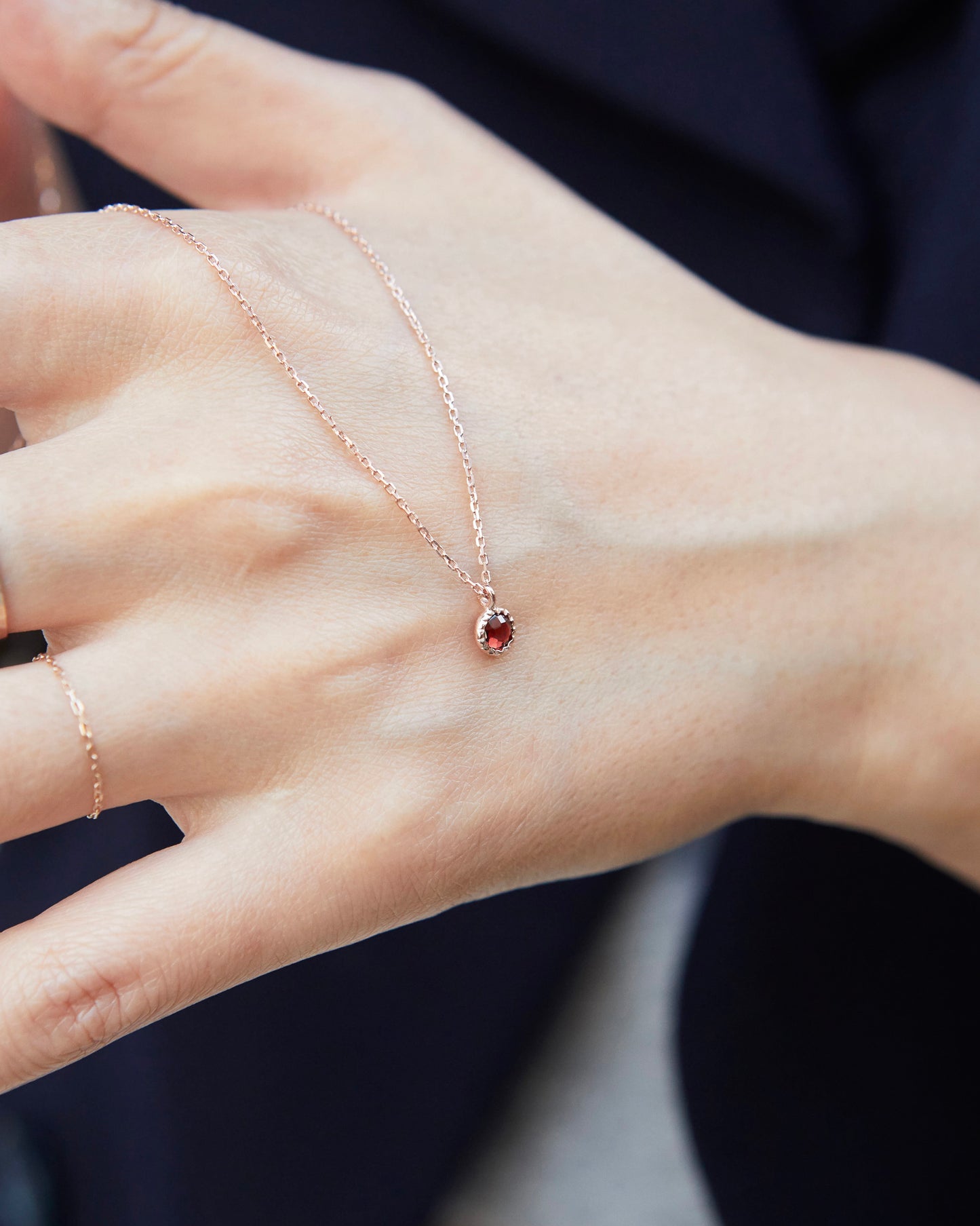 Rose gold necklace with a red gemstone on a hand against a dark background
