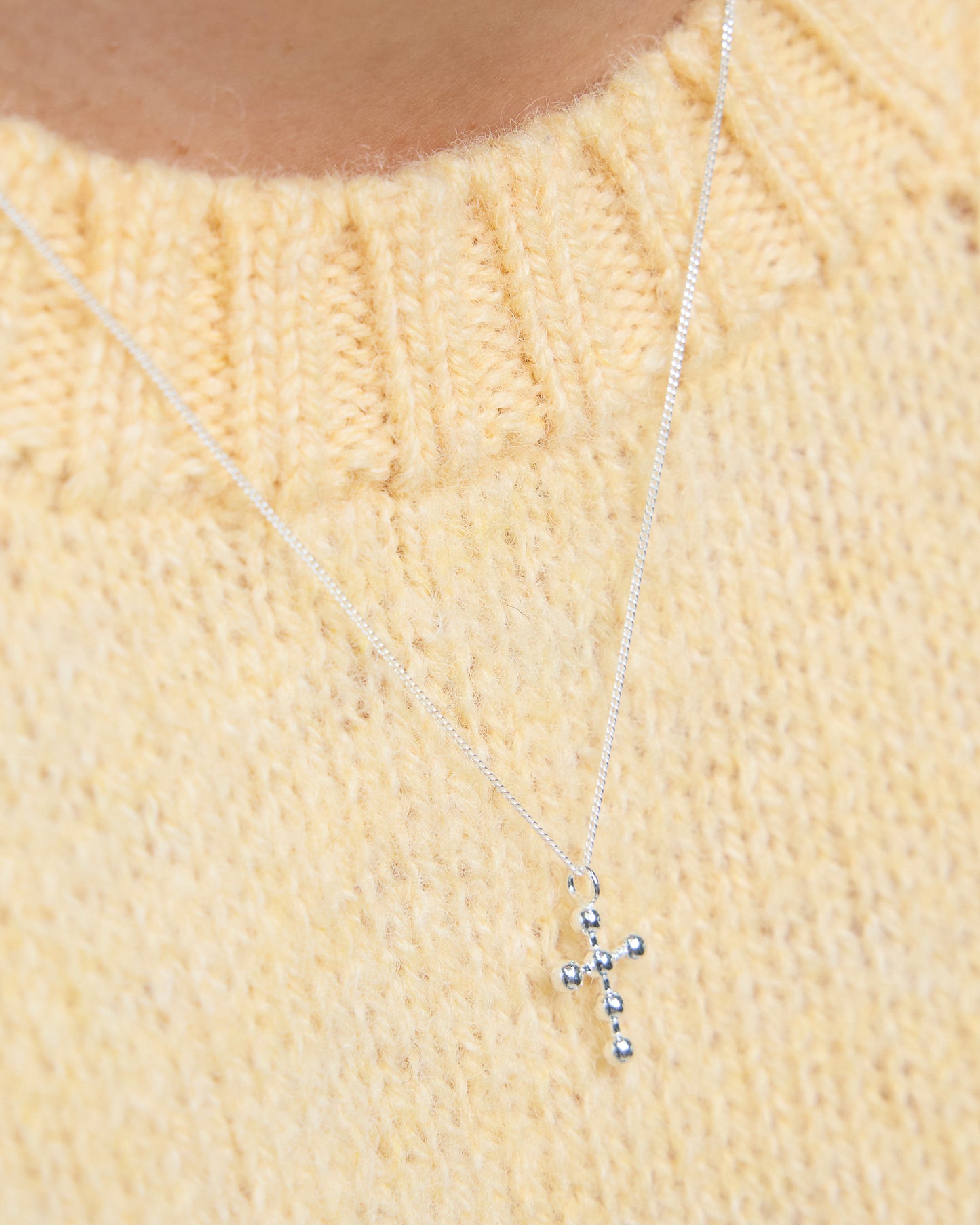 Close-up of silver cross necklace with beaded accents, worn over soft yellow knit