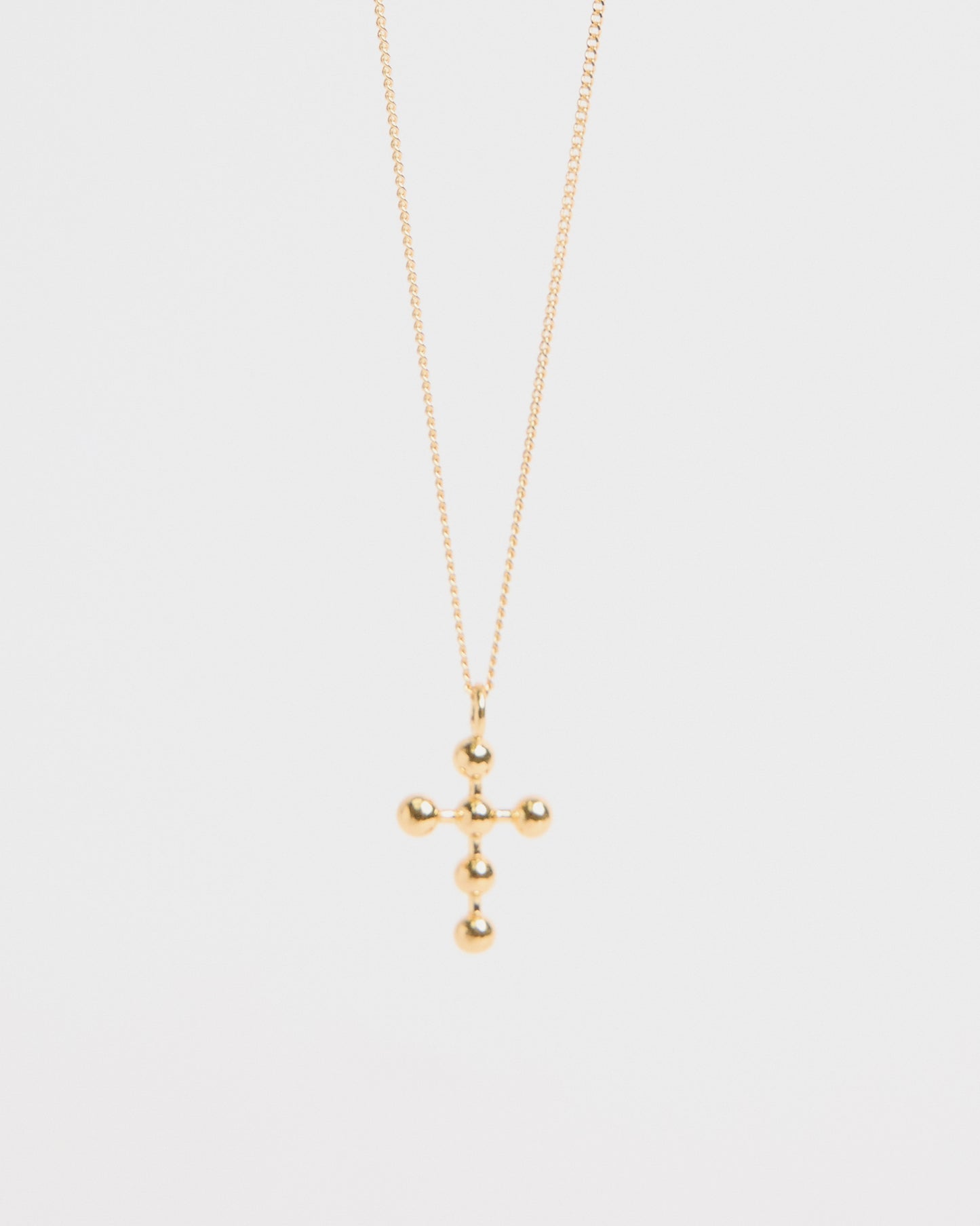 Centered image of gold beaded cross pendant necklace against white backdrop