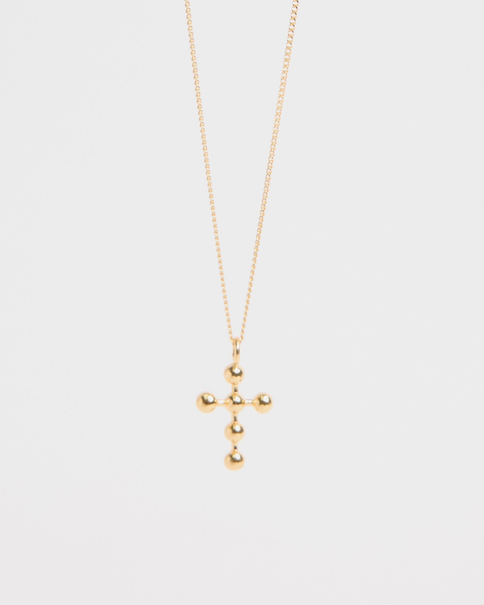 Centered image of gold beaded cross pendant necklace against white backdrop