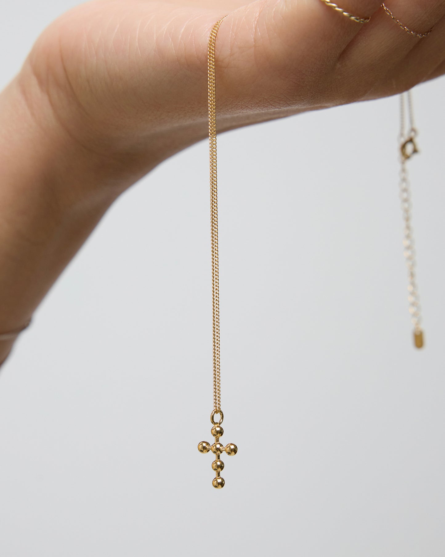 Hand holding delicate gold beaded cross necklace with fine chain