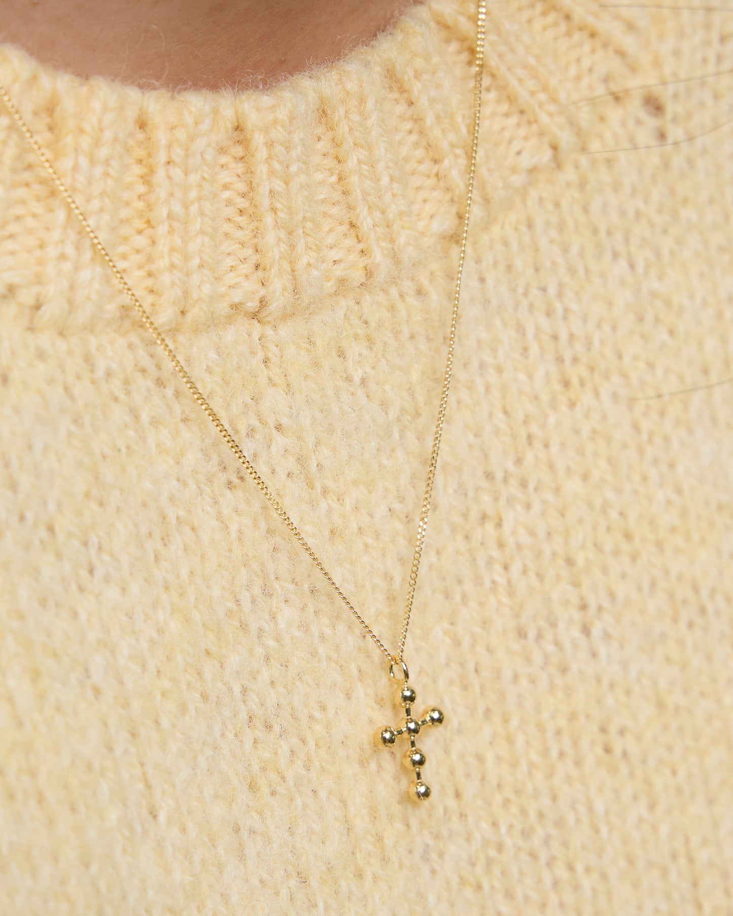 Gold cross necklace worn with cozy yellow knit, subtle and centered.
