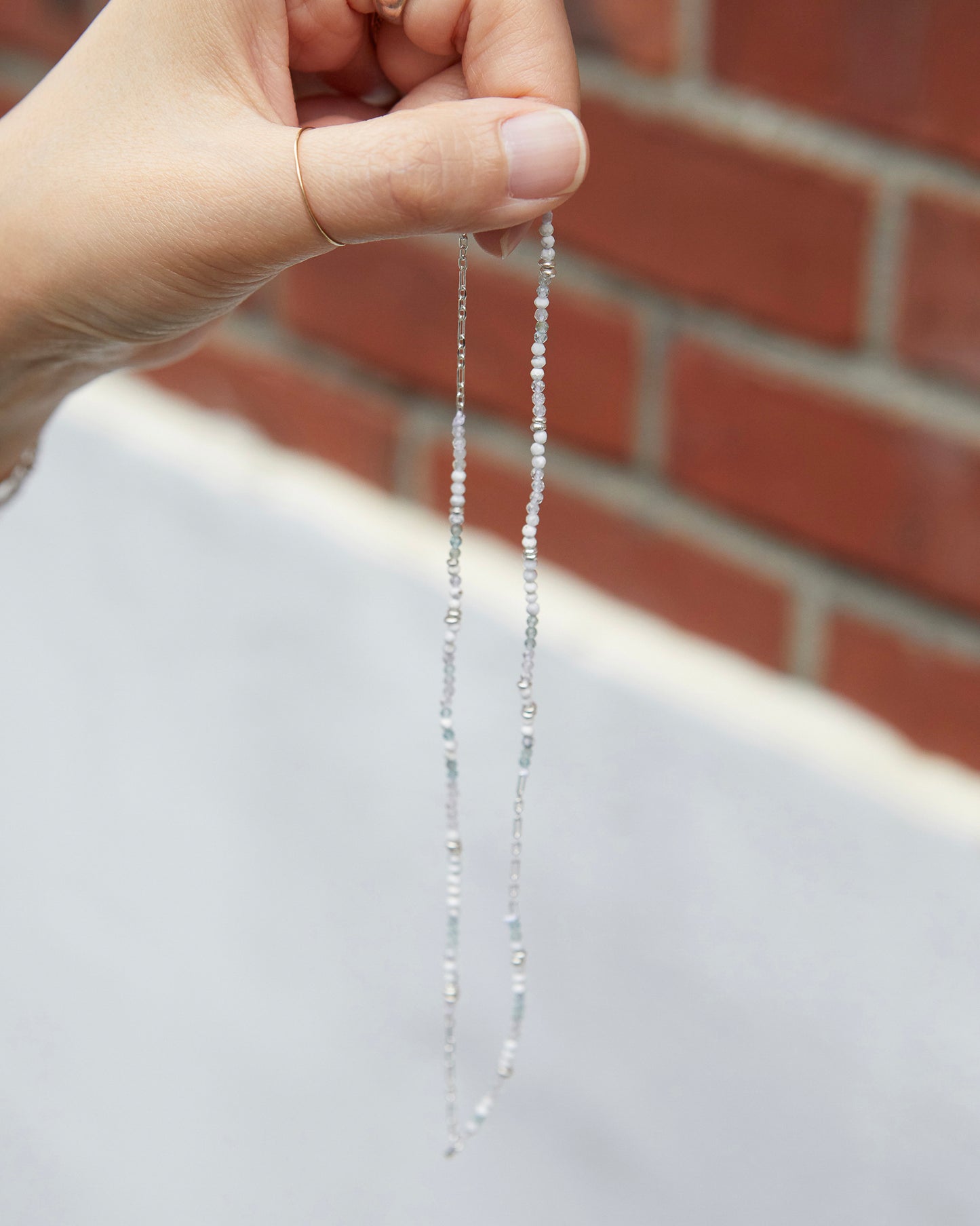 hand holding a dainty beaded necklace in natural outdoor lighting