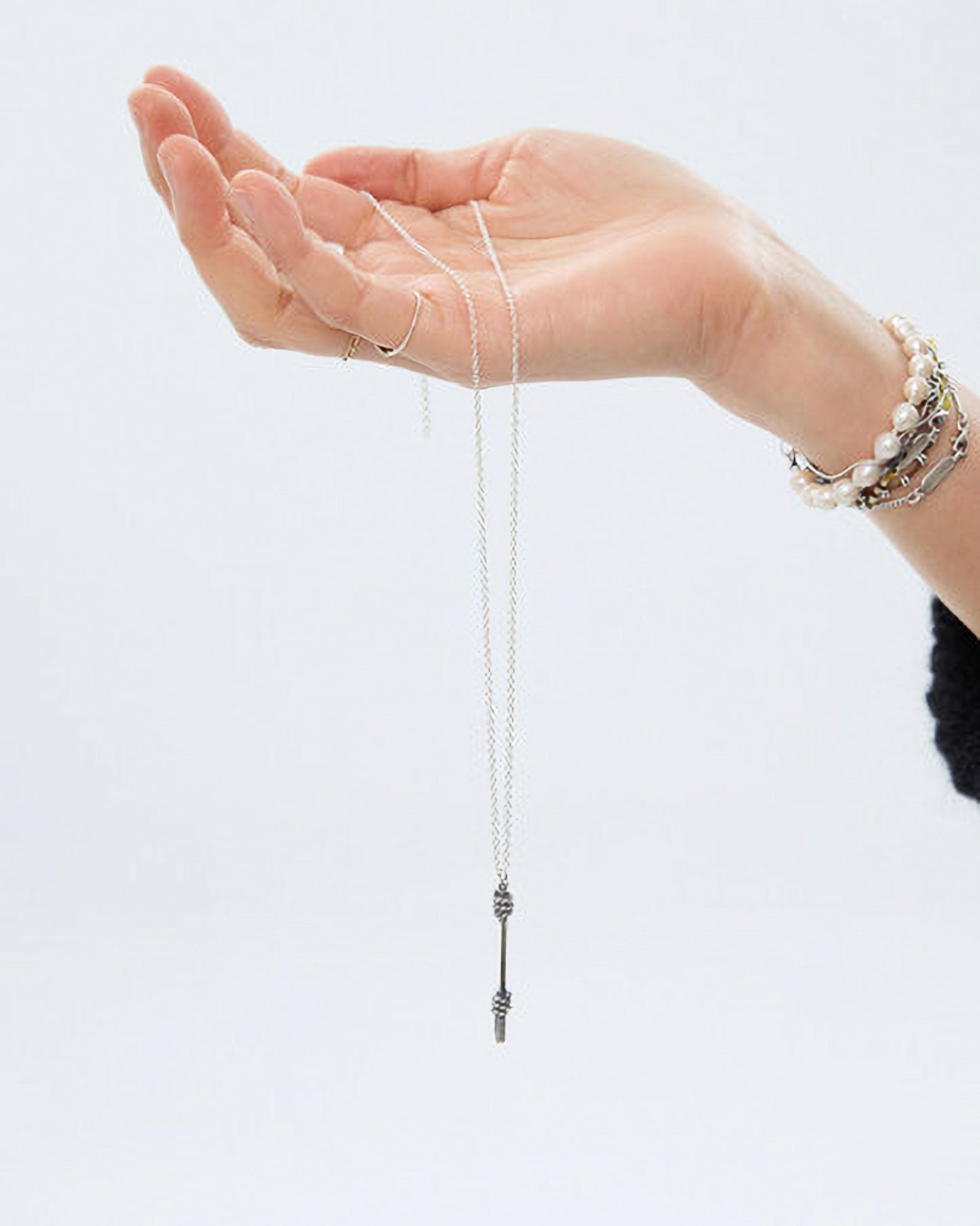 Hand holding a silver necklace against a white background