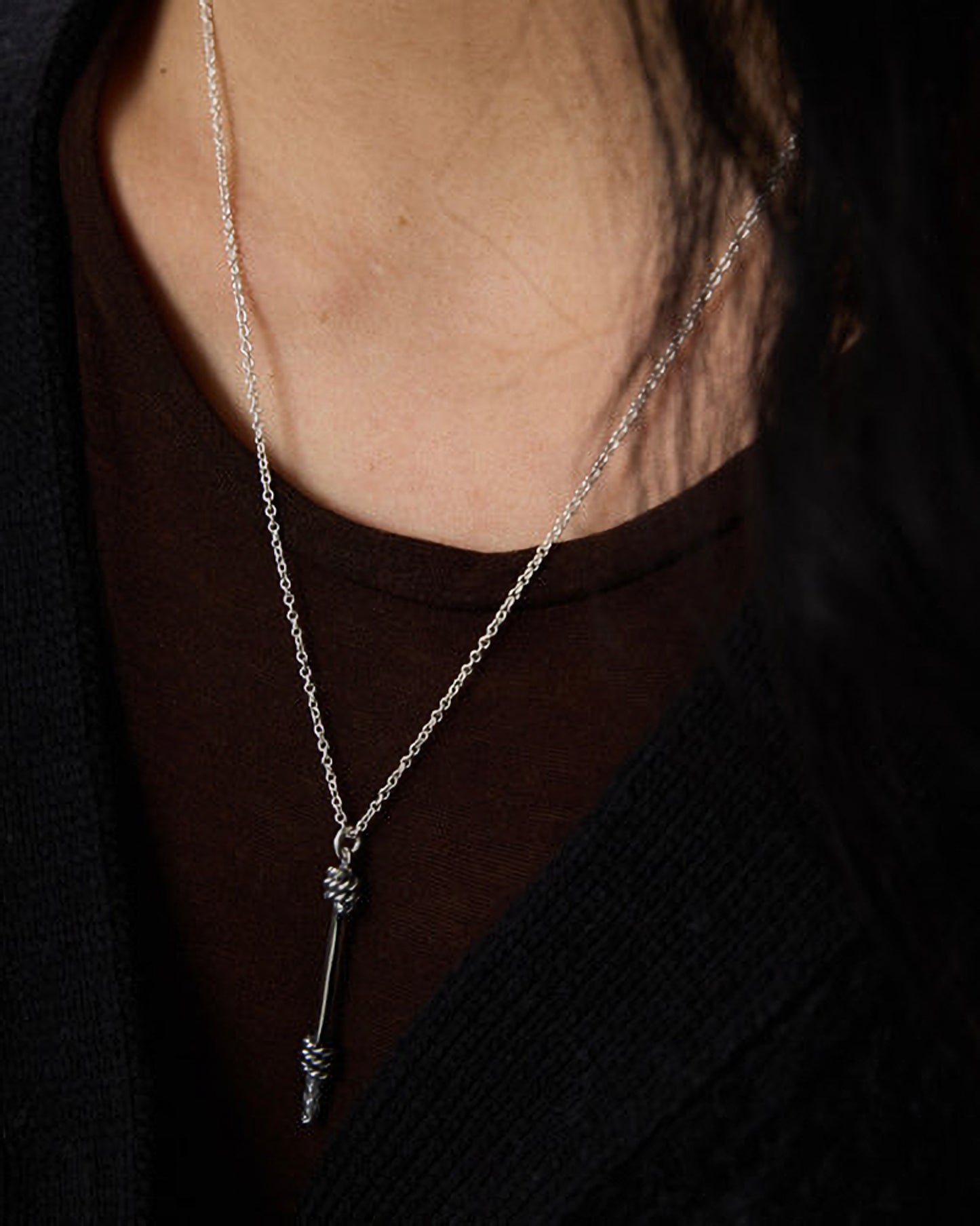 Silver necklace with a pendant worn by a person against a dark background