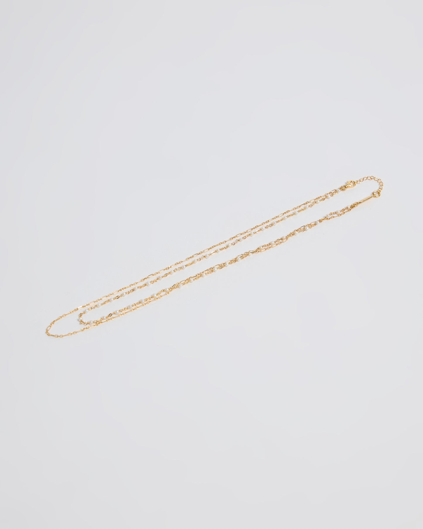 gold necklaces laid flat showing a pearl chain and a simple chain combination