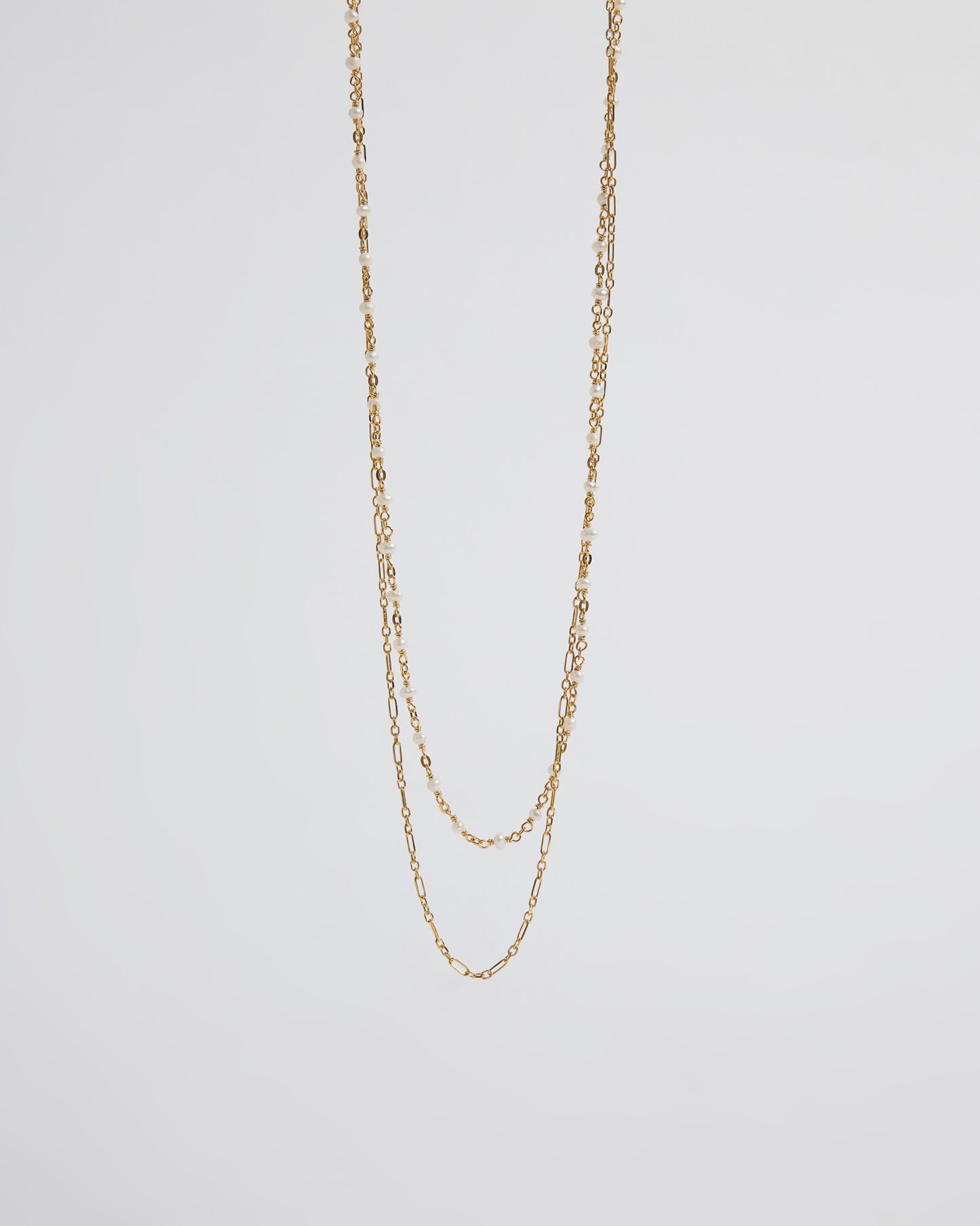 a long layered necklace draped over the hand showing pearl and chain contrast