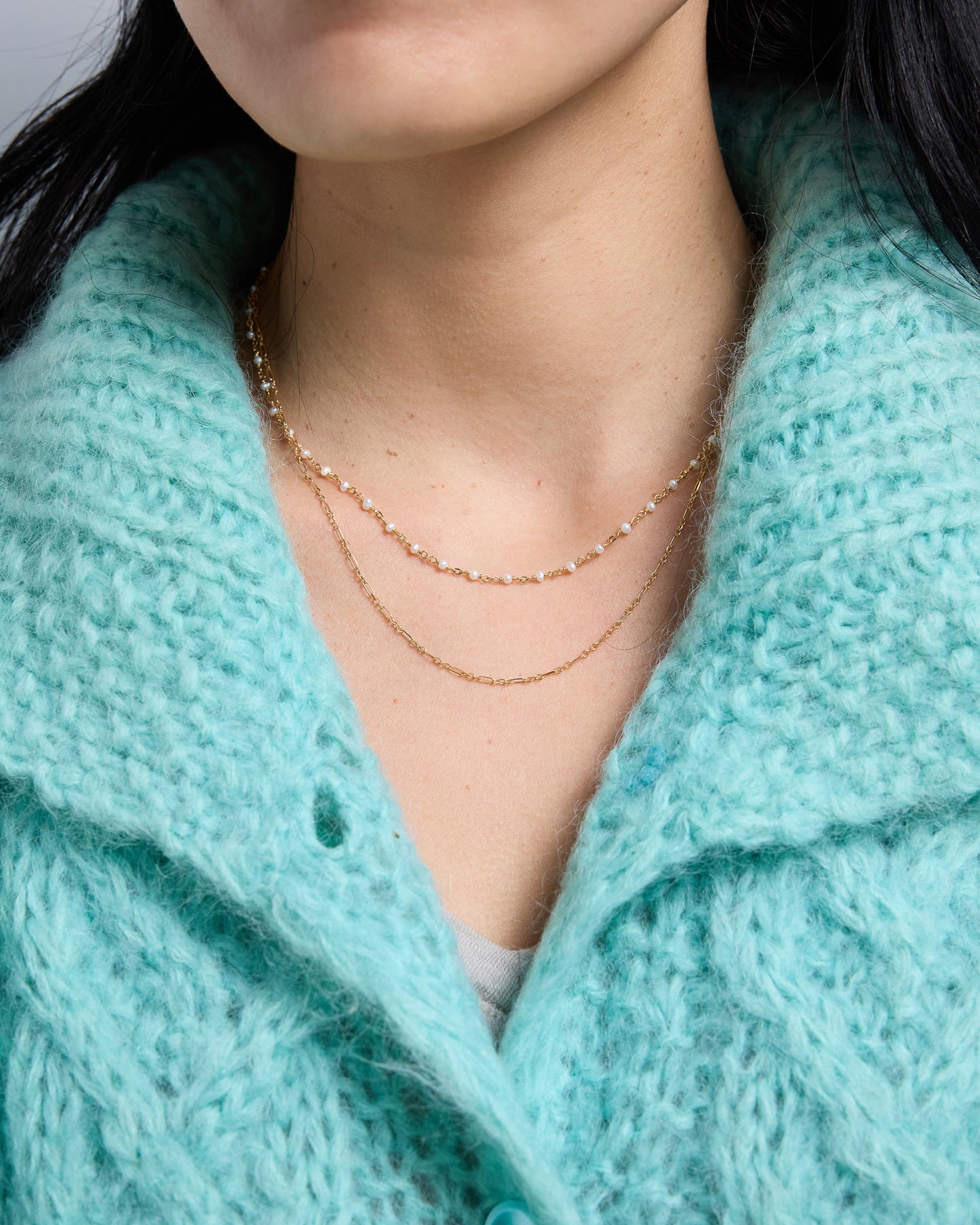 a layered necklace with a pearl chain and a simple gold chain worn together on the neck