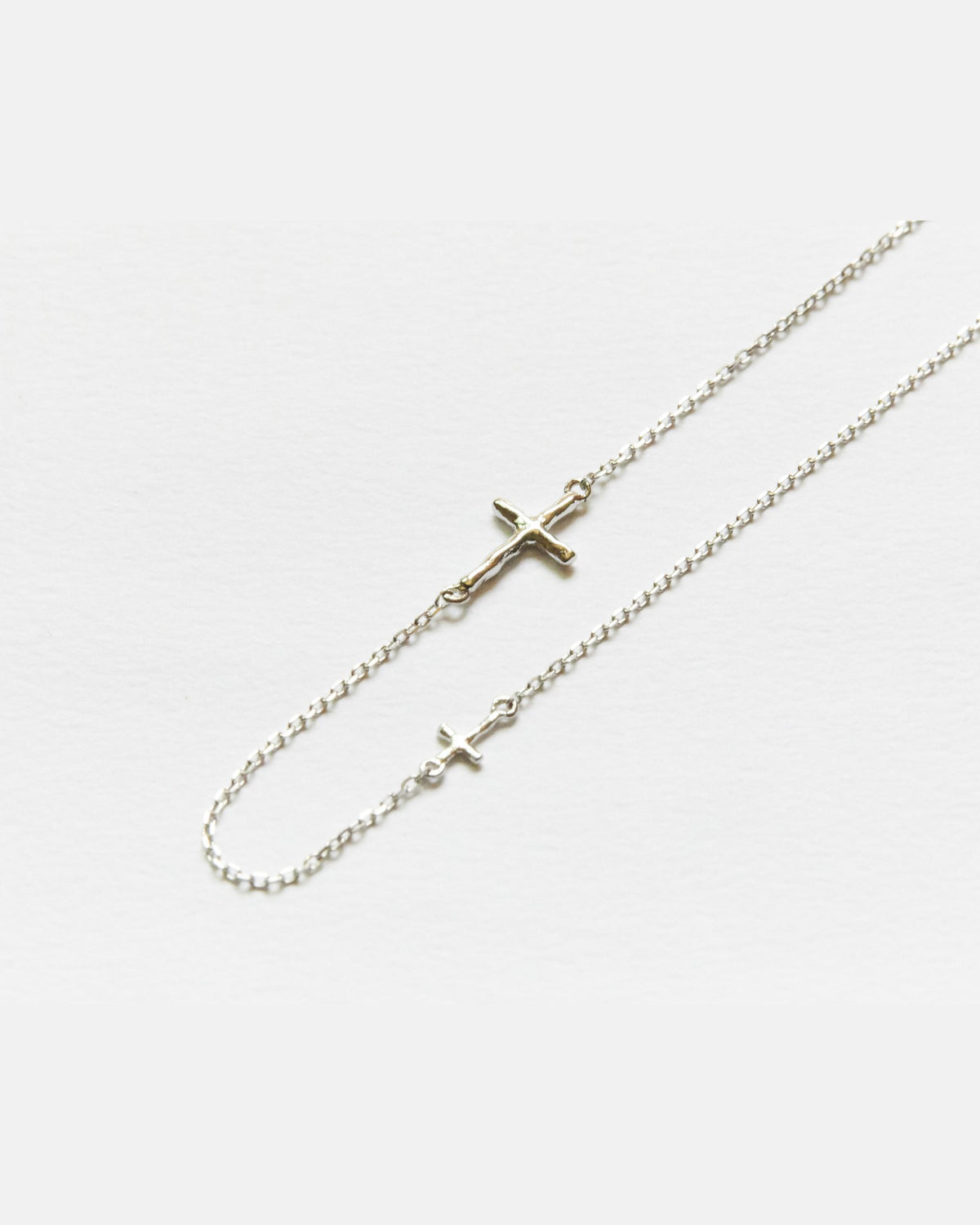 Close-up of two small silver crosses on a fine chain necklace – HANNA543 N314 twin cross chain