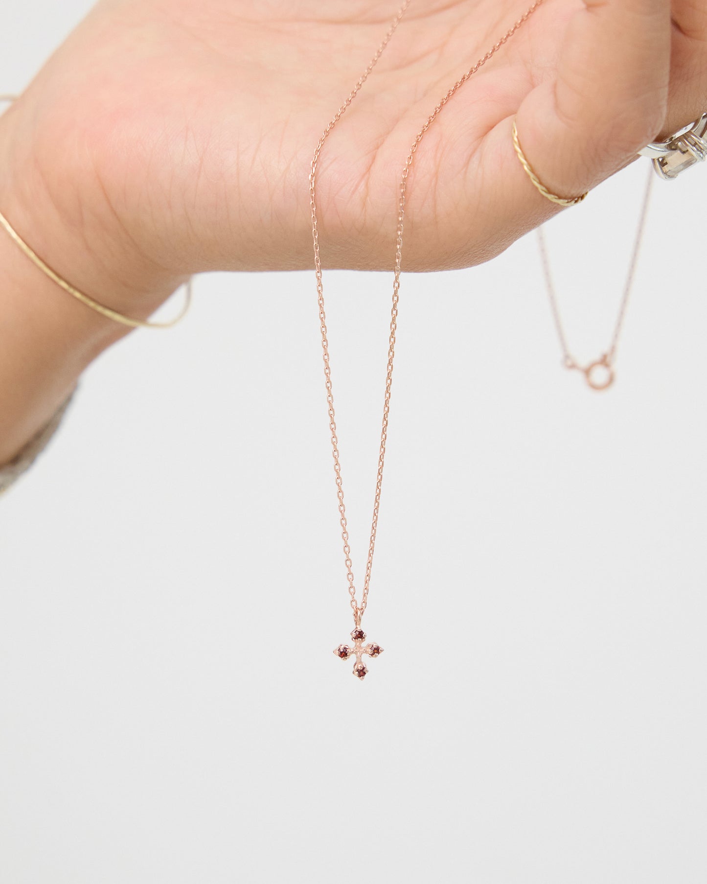 Rose gold necklace with a small pendant held by a hand on a light background